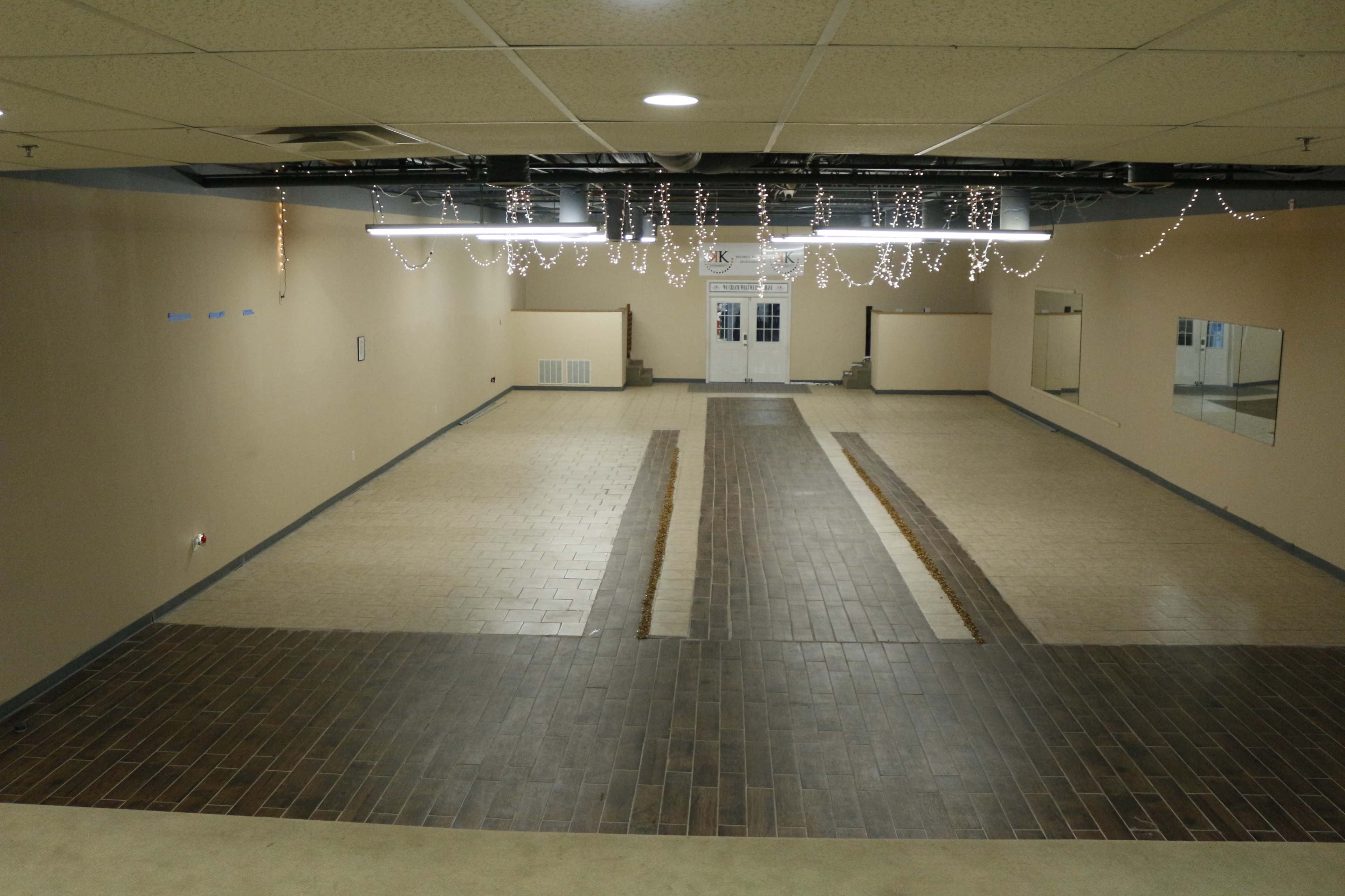 A spacious room with tiled flooring and ceiling decorations, featuring a central pathway leading to double doors at the far end.
