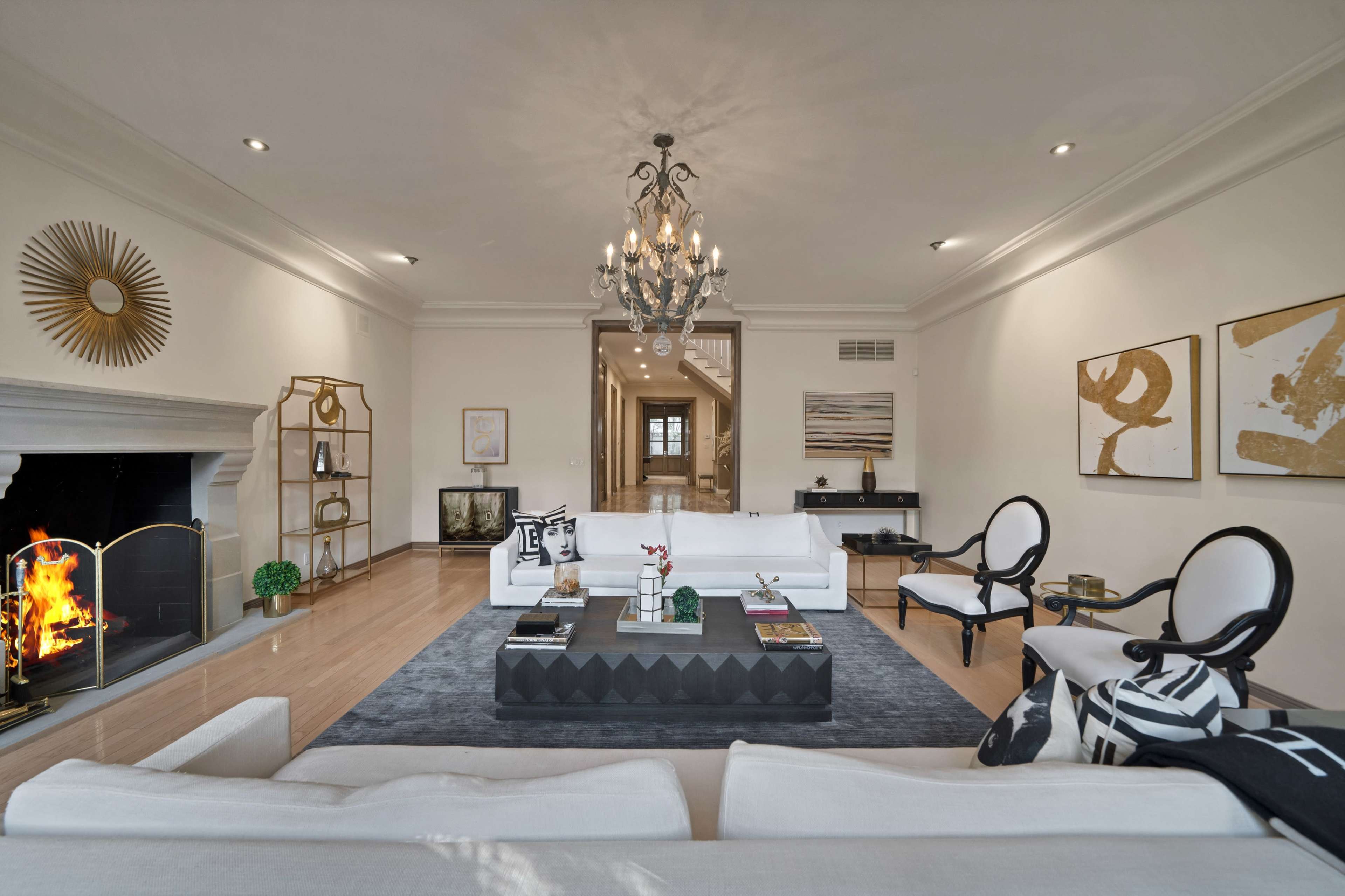 The spacious living room features a central coffee table, two stylish chairs, and a fireplace, with artwork and decorative elements arranged throughout.