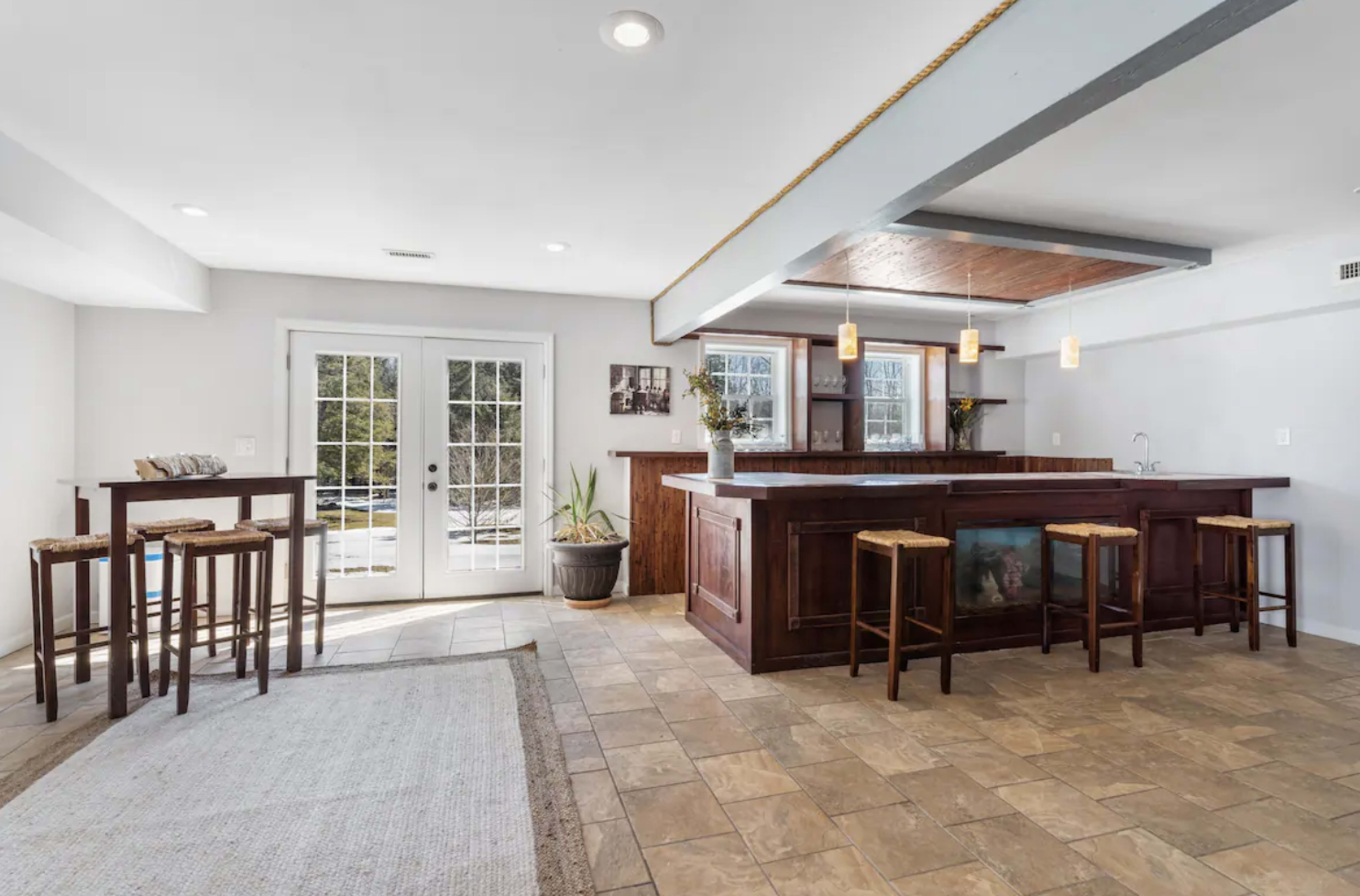 The image shows a spacious interior with a wooden bar, high stools, and large glass doors leading to the outdoors.