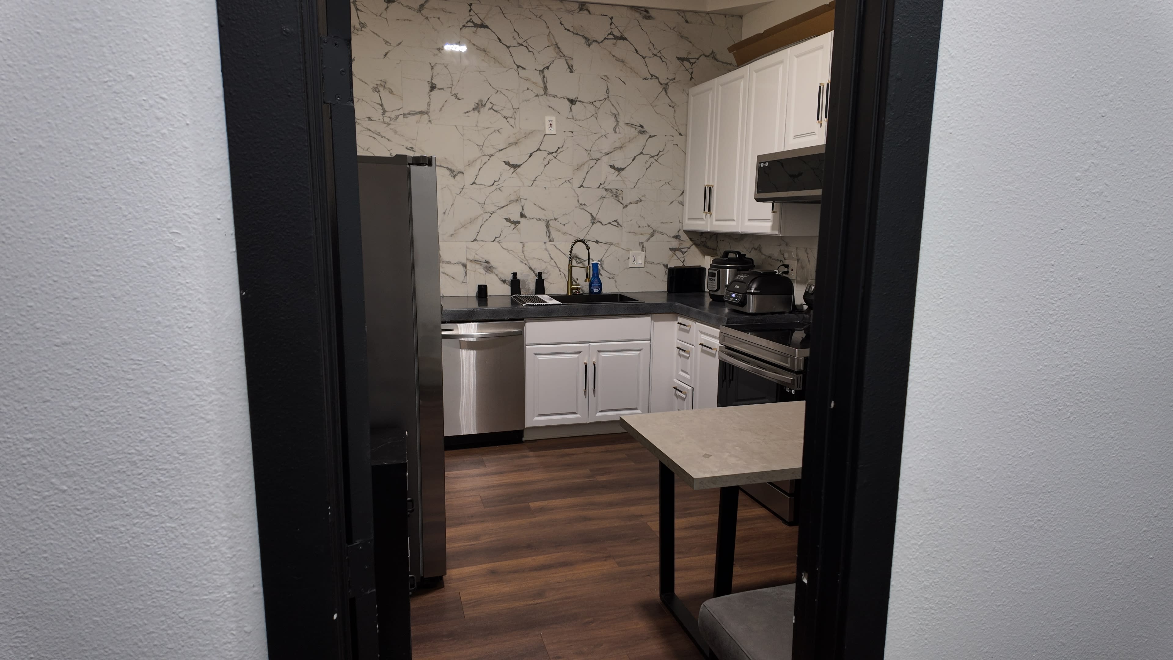 A modern kitchen features white cabinets, a stainless steel refrigerator, and a marble backsplash with dark countertops.