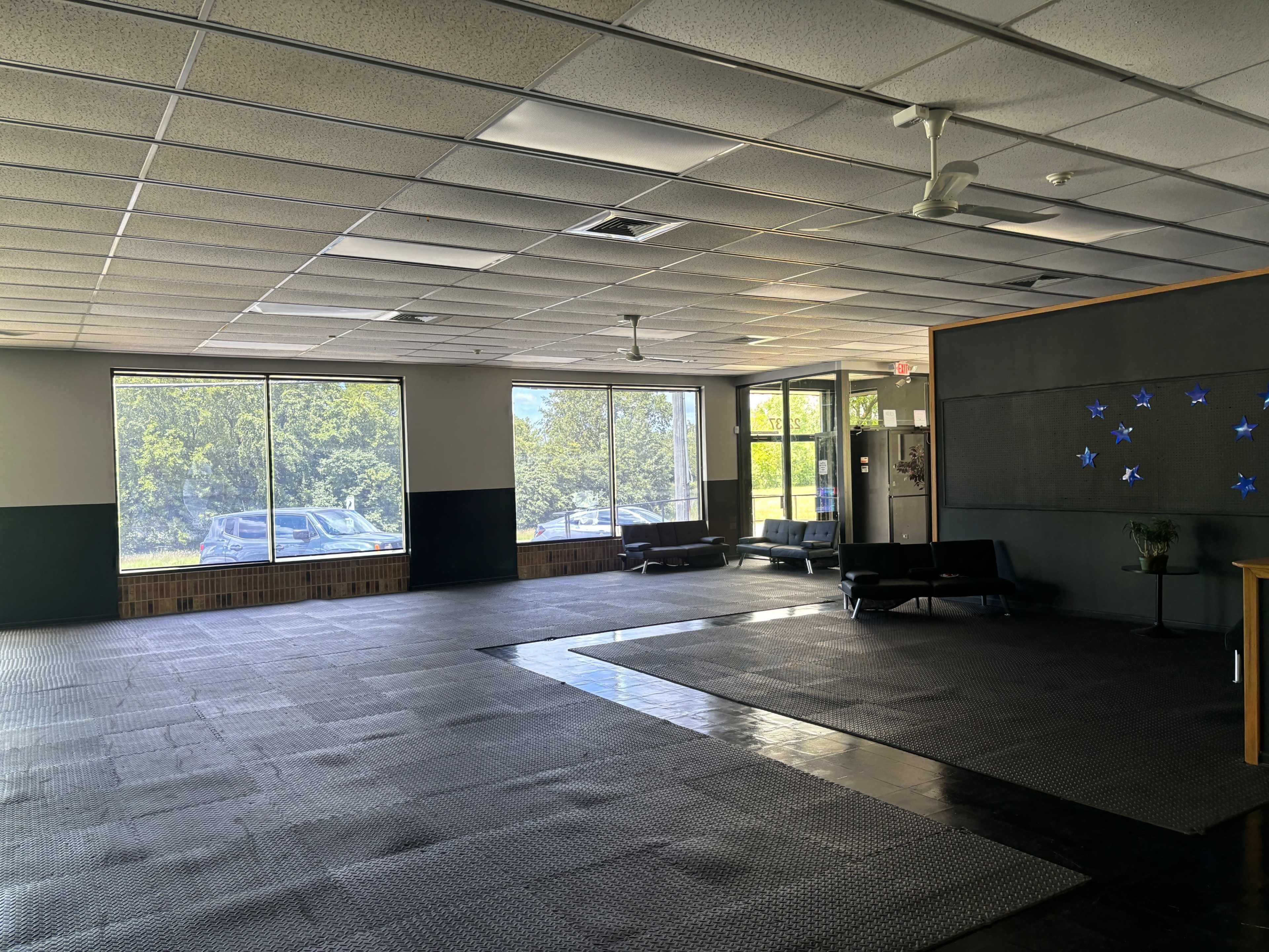 The image shows an empty, spacious room with large windows, a black tile floor, and a few pieces of furniture along the walls.