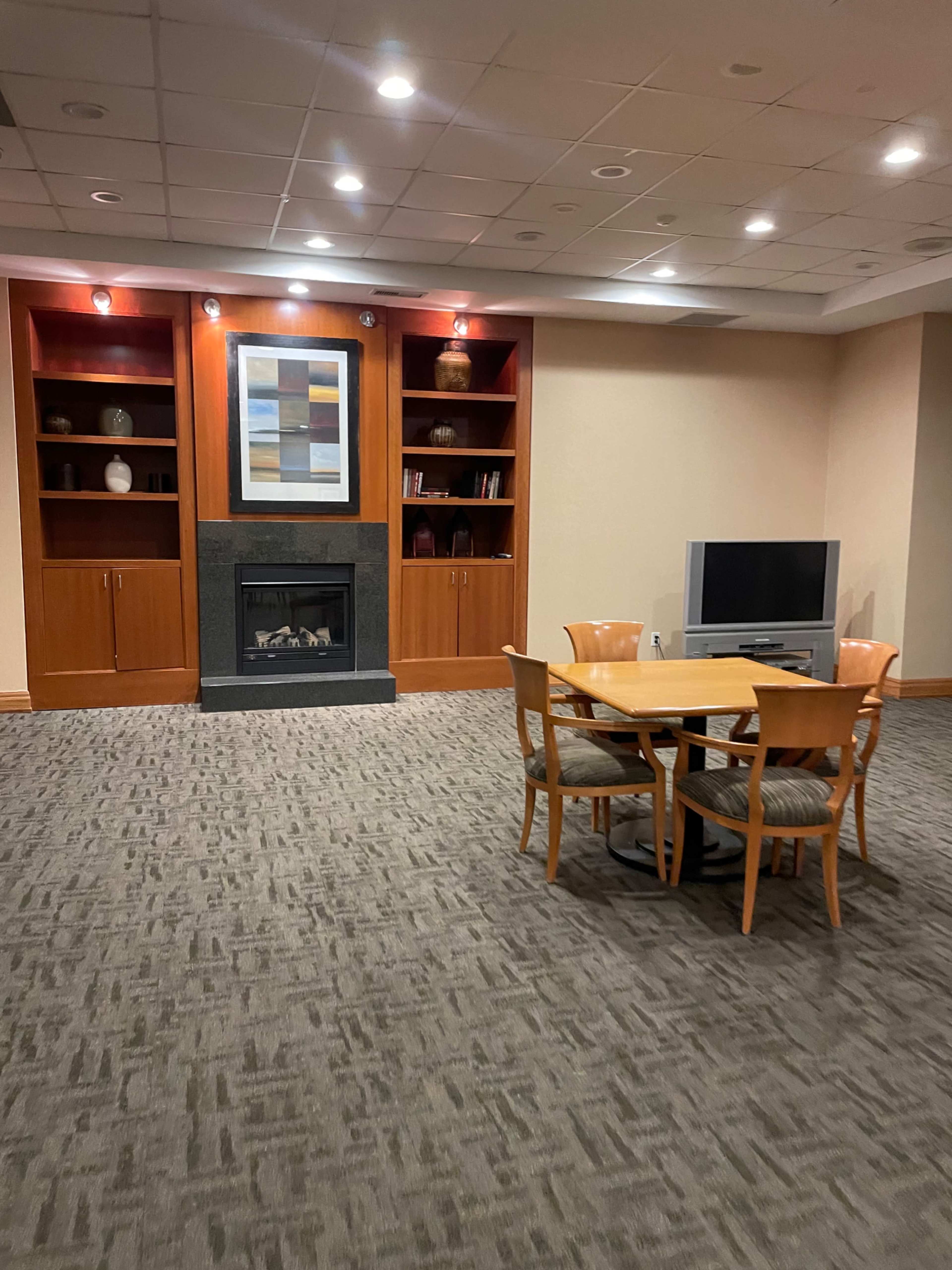 A spacious lounge area featuring a fireplace, built-in shelves with decorative items, and a table with four chairs positioned in the center.