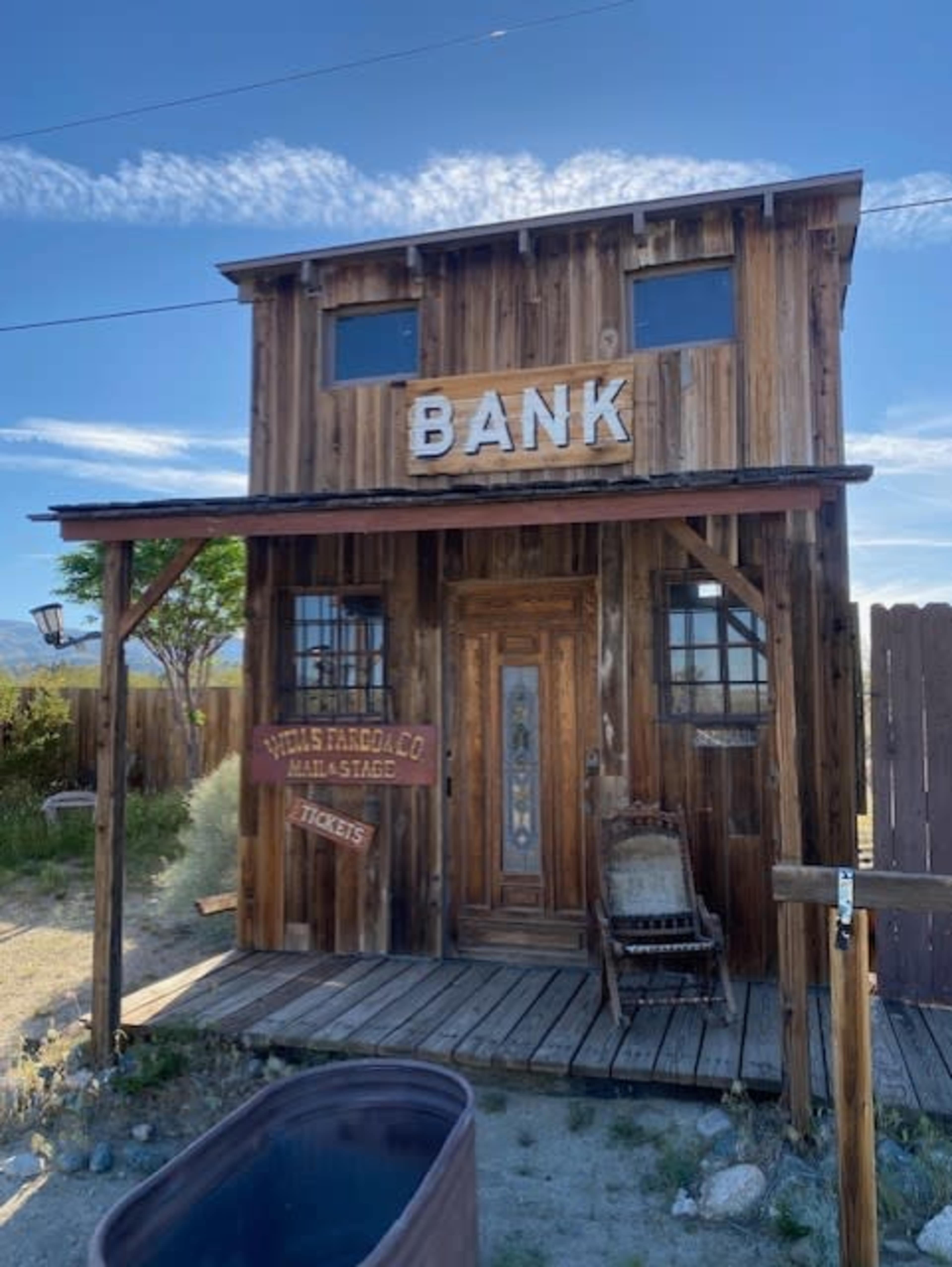 The image shows a vintage wooden building labeled "BANK," featuring a porch and a sign that reads "HILLS FARGO & CO. MAIL & STAGE."