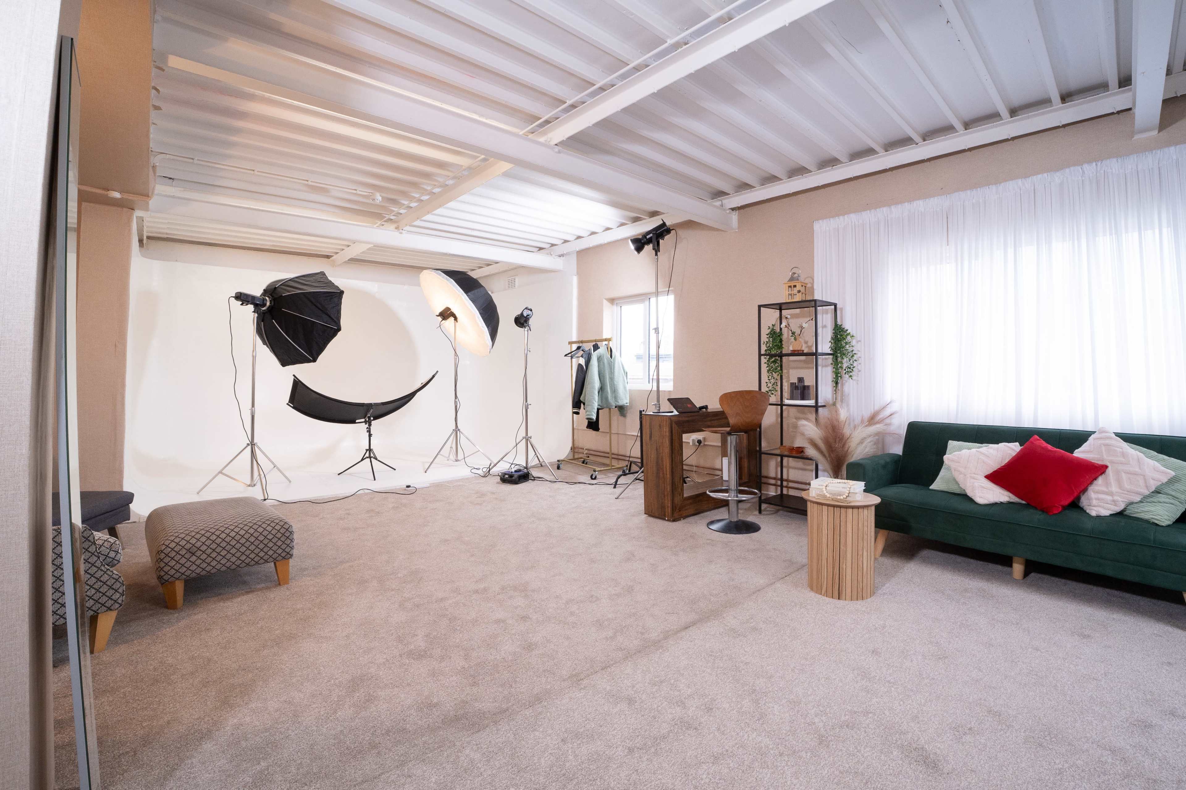 The image shows a photography studio with a green sofa, a table, and lighting equipment set up against a white backdrop.