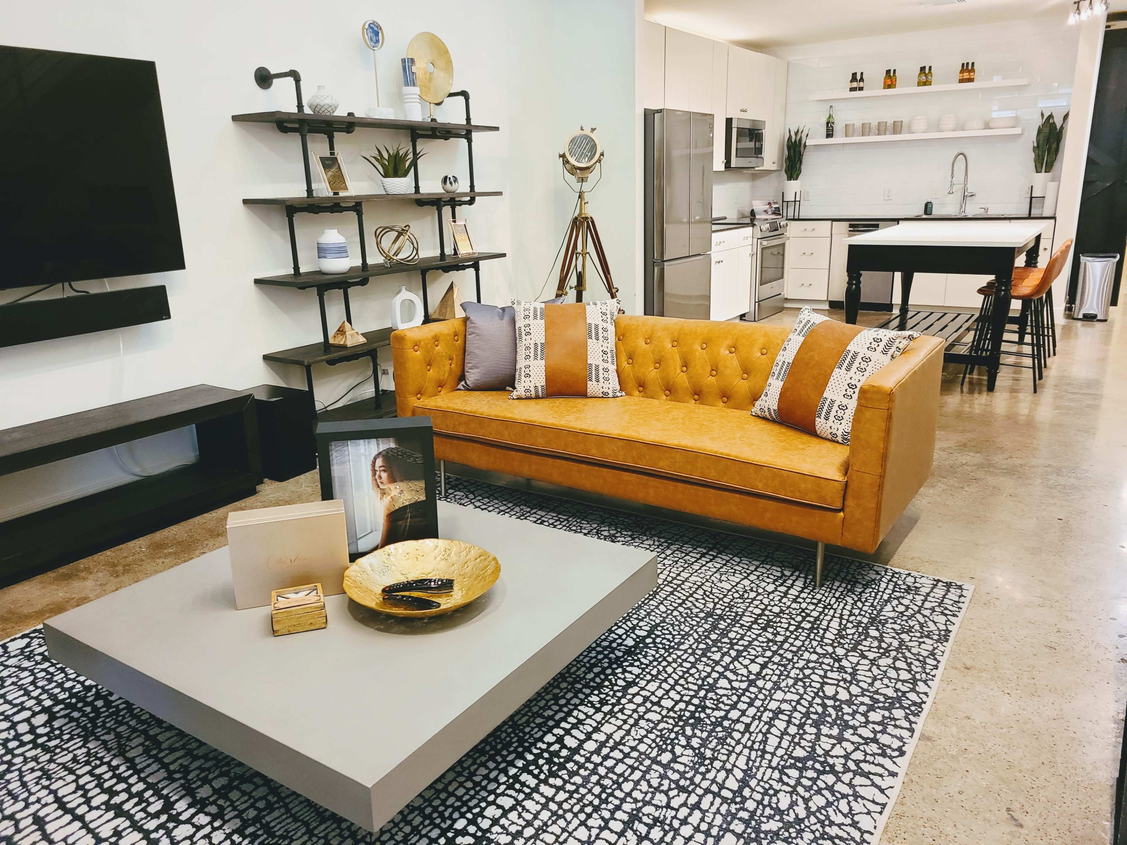 A modern living room with a mustard-colored sofa, a coffee table, and an open kitchen in the background.