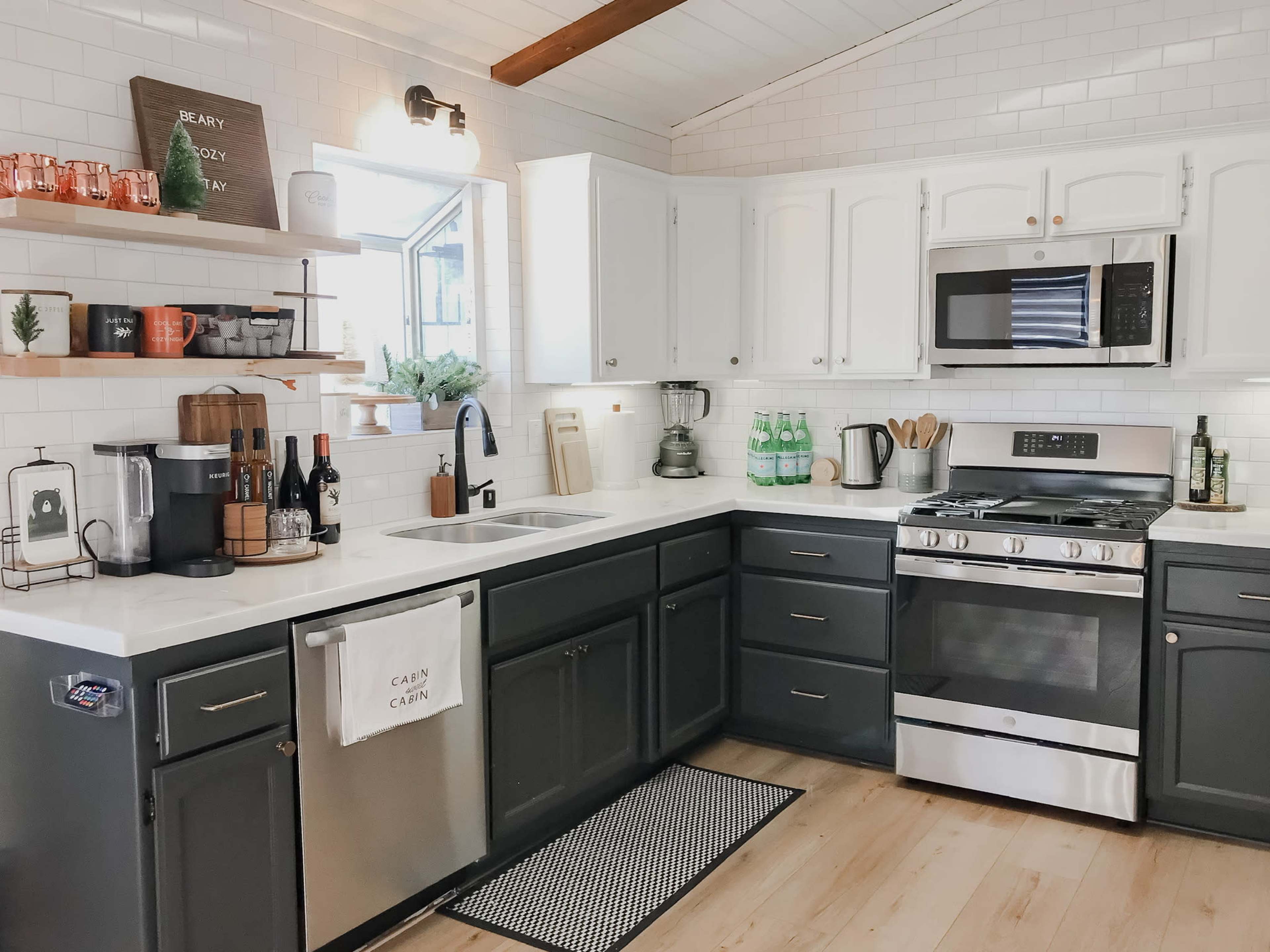 The image shows a modern kitchen with white cabinets, a stainless steel stove, and a gray island, featuring various kitchen appliances and decorative items on the shelves.