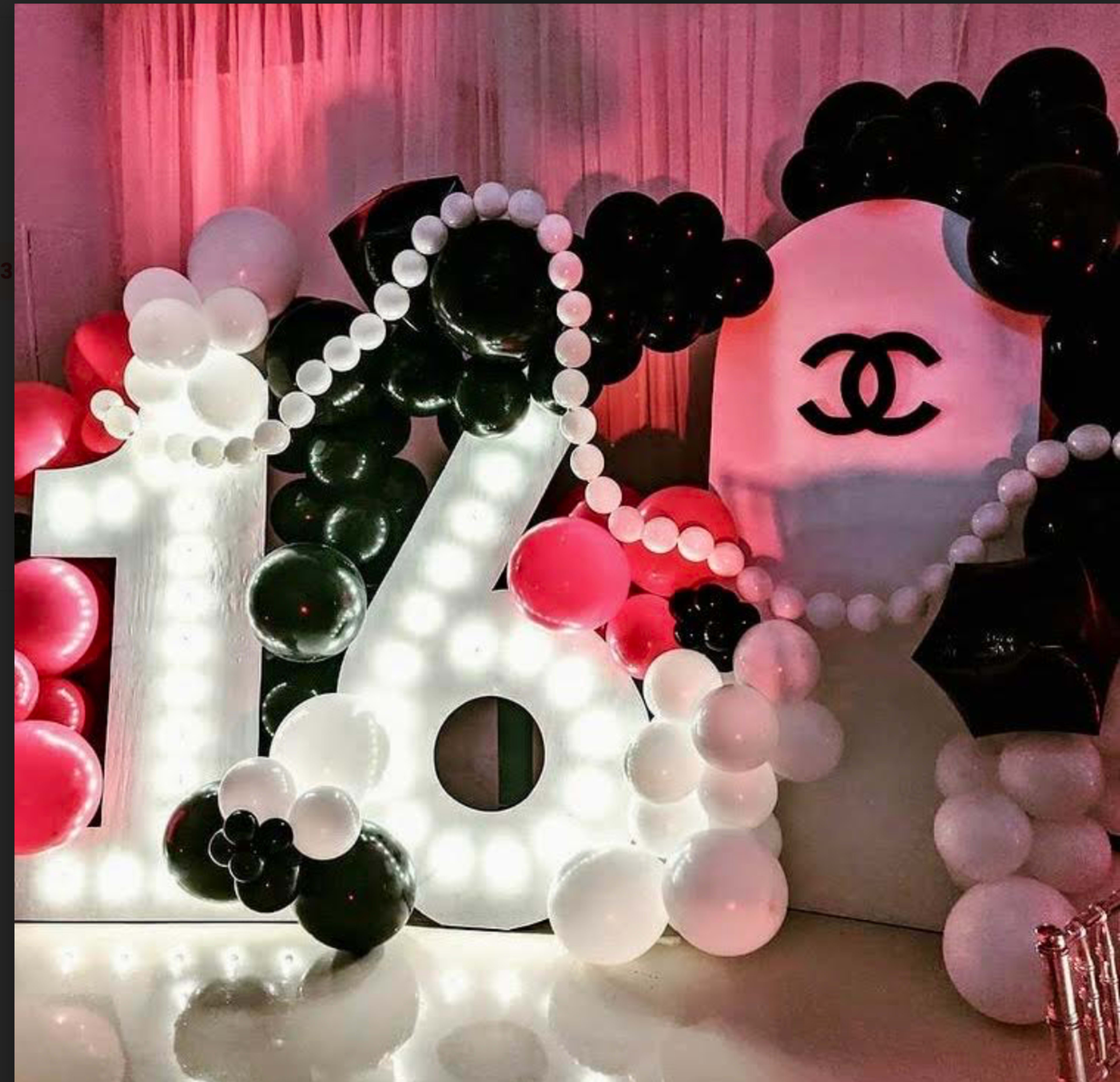 The image features a large, illuminated "16" made of balloons, surrounded by black and white balloons, and displays a Chanel logo in the background.