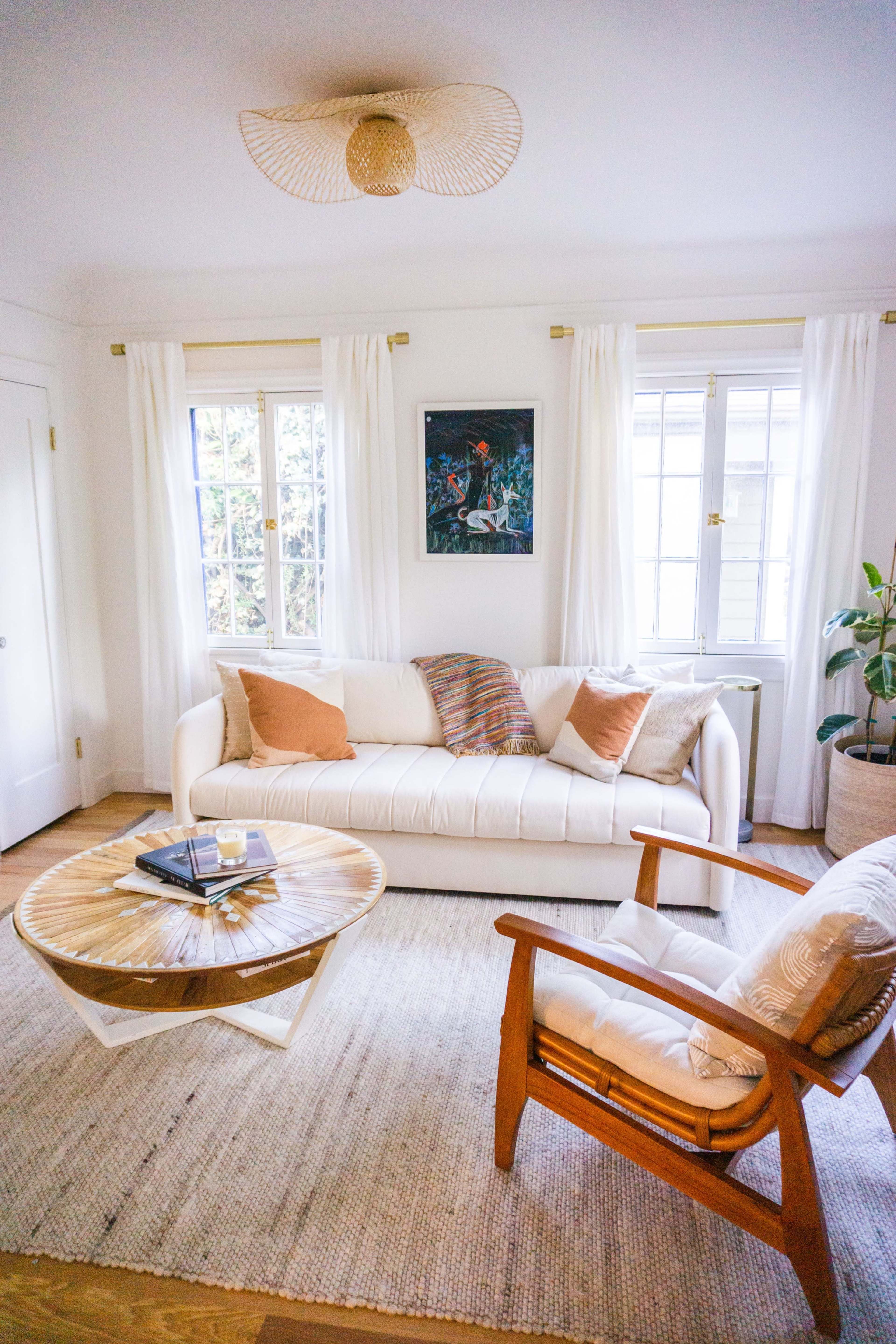 A cozy living room with a white sofa, a wooden coffee table, and a lounge chair, adorned with plants and soft natural light.