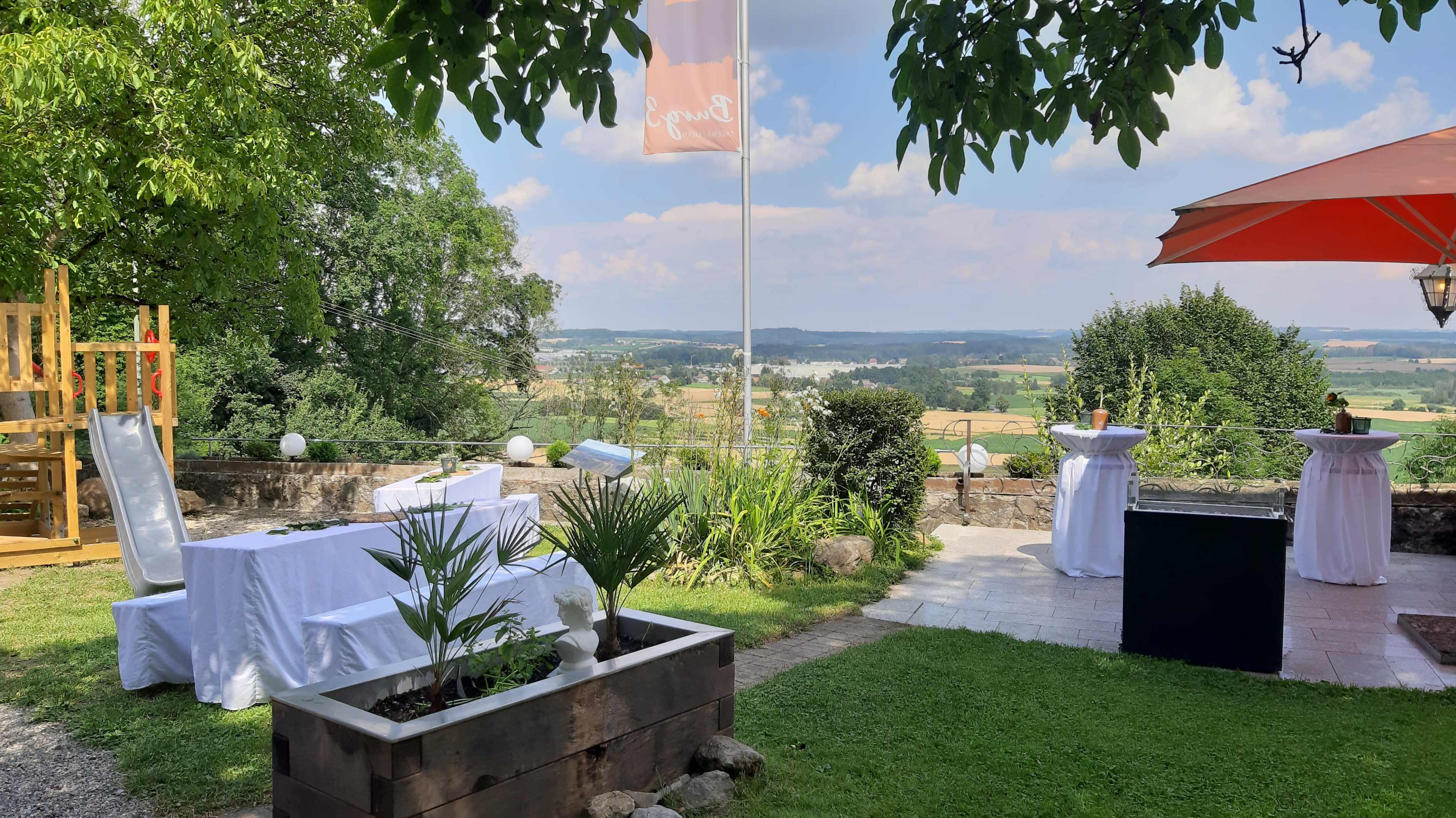 The image shows a landscaped outdoor area with tables and decorations overlooking a scenic valley.