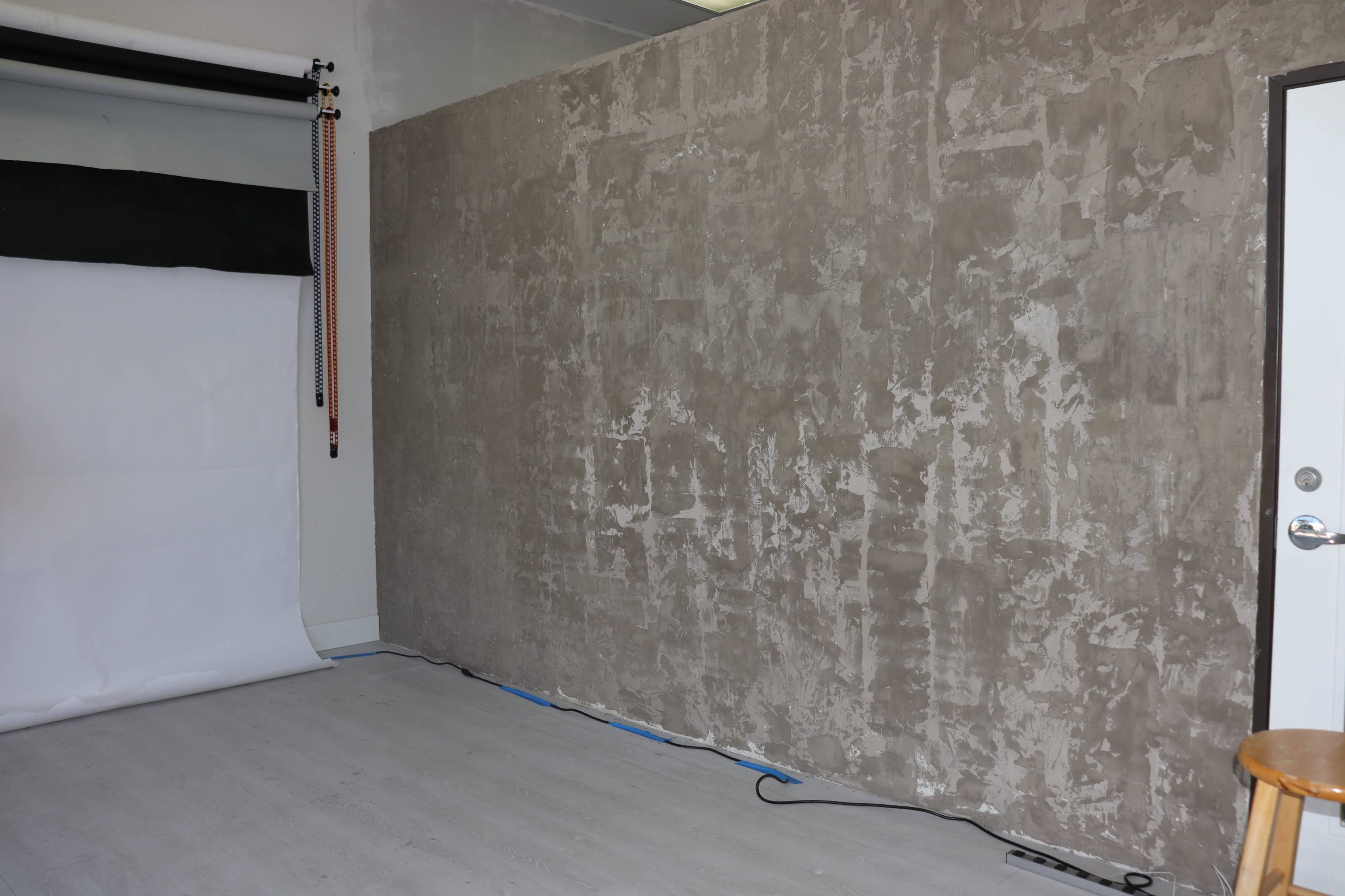 A studio setting with a textured concrete wall, a roll of white paper backdrop, and a door on one side.