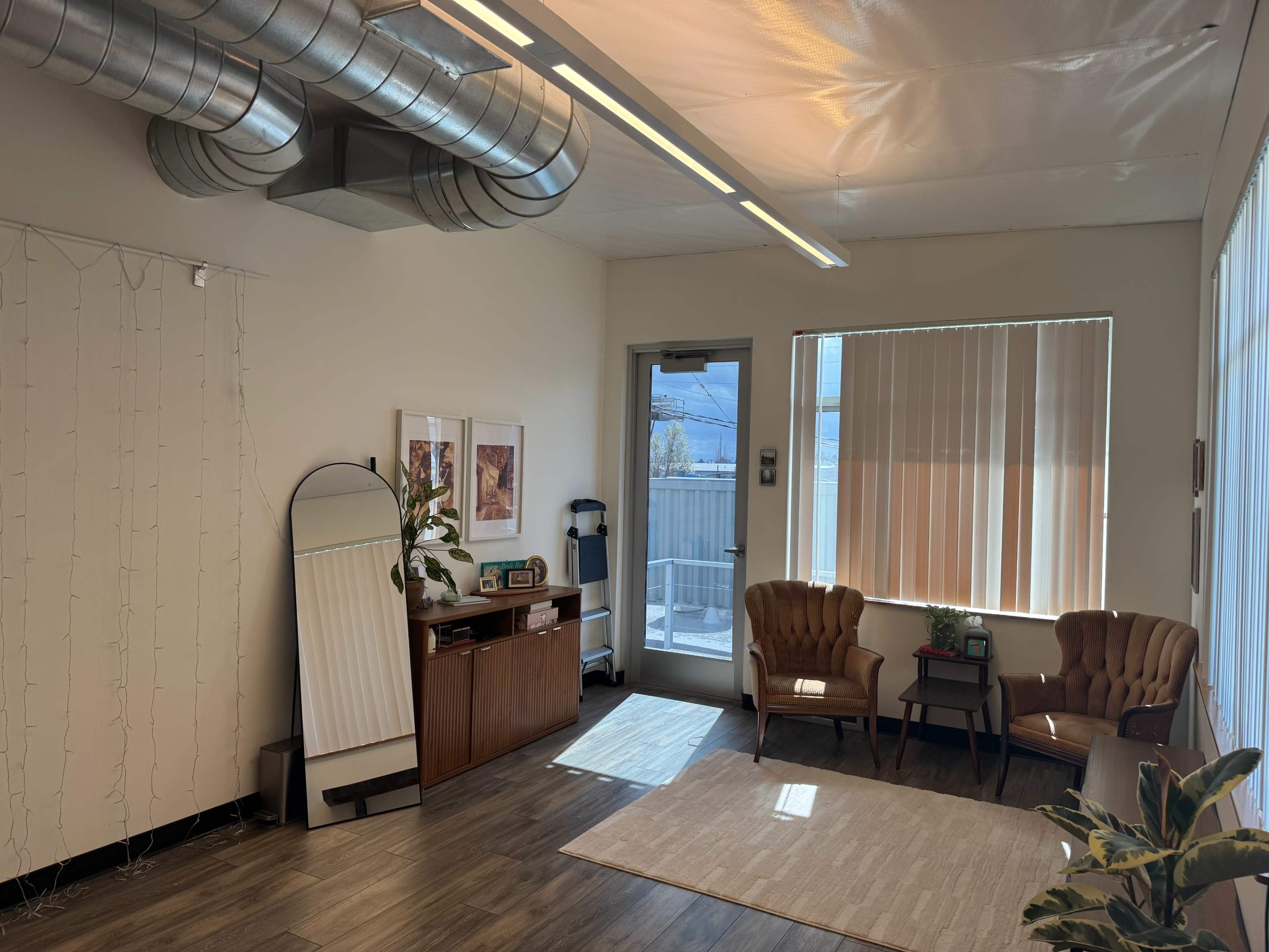 The image shows a well-lit waiting area featuring two armchairs, a wooden cabinet, and an abstract wall decor, with large windows revealing a snowy outdoor scene.