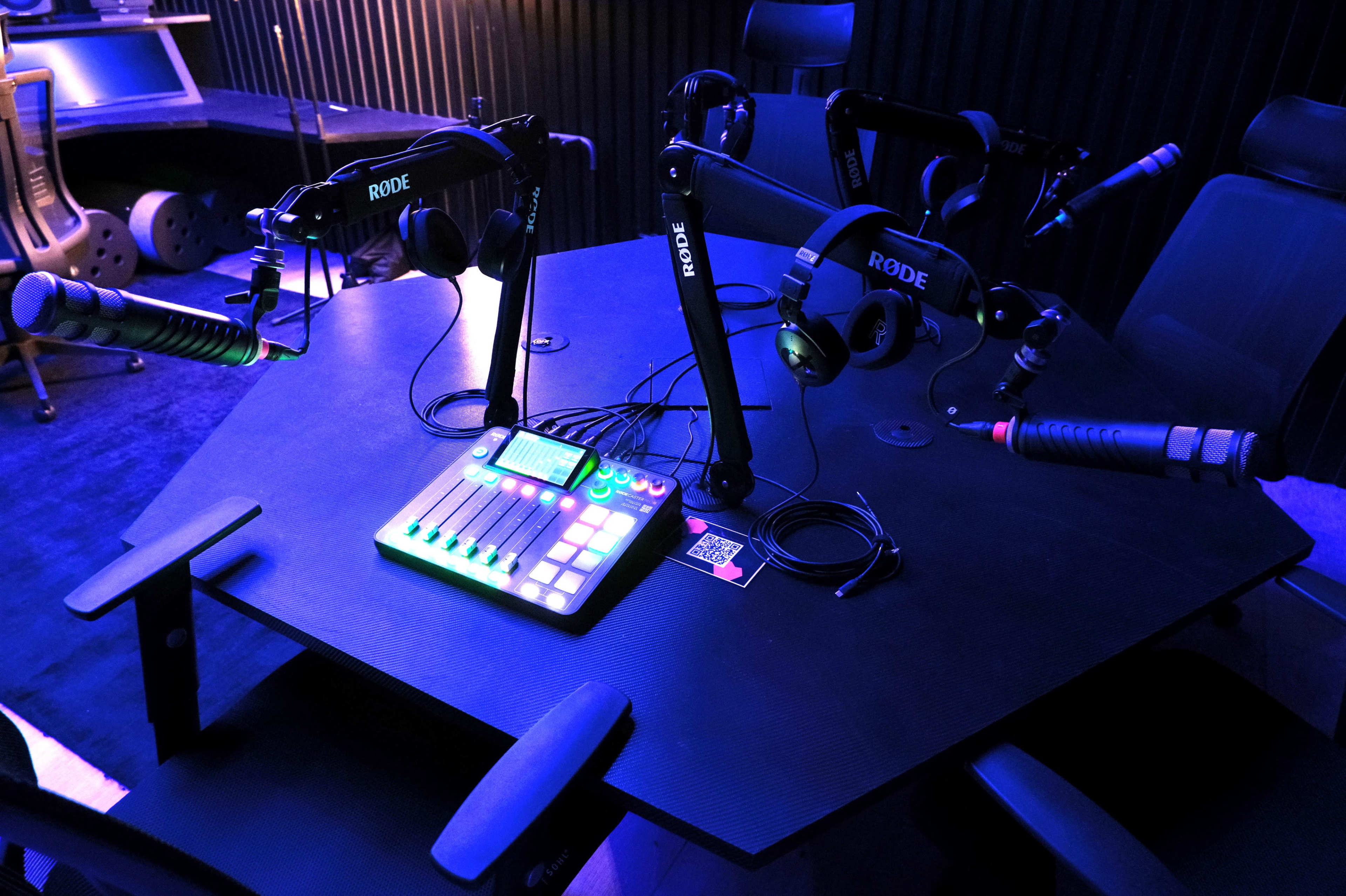The image shows a recording studio with an octagonal table equipped with multiple microphones and headphones.