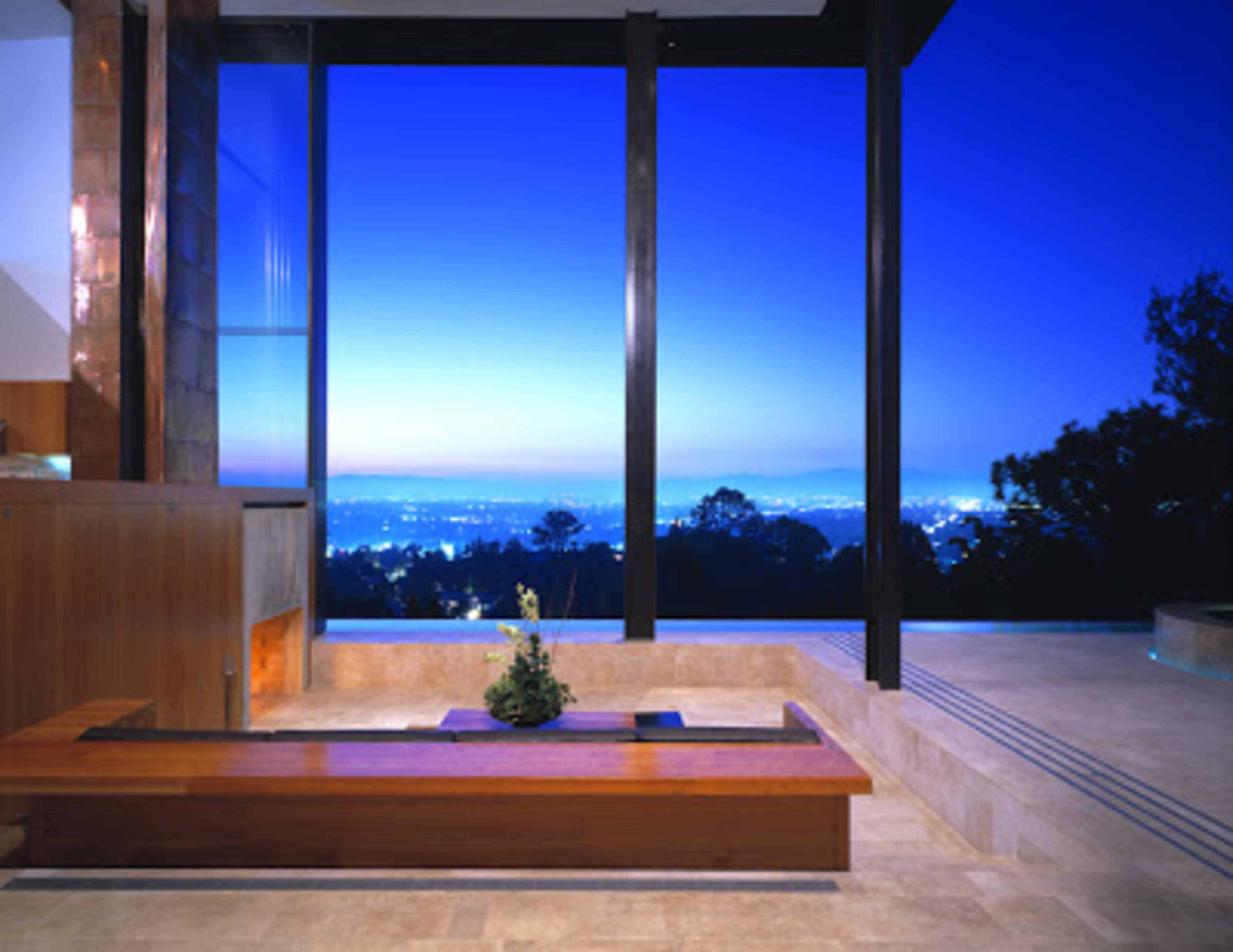 A modern indoor space with large glass windows overlooking a city skyline at twilight.