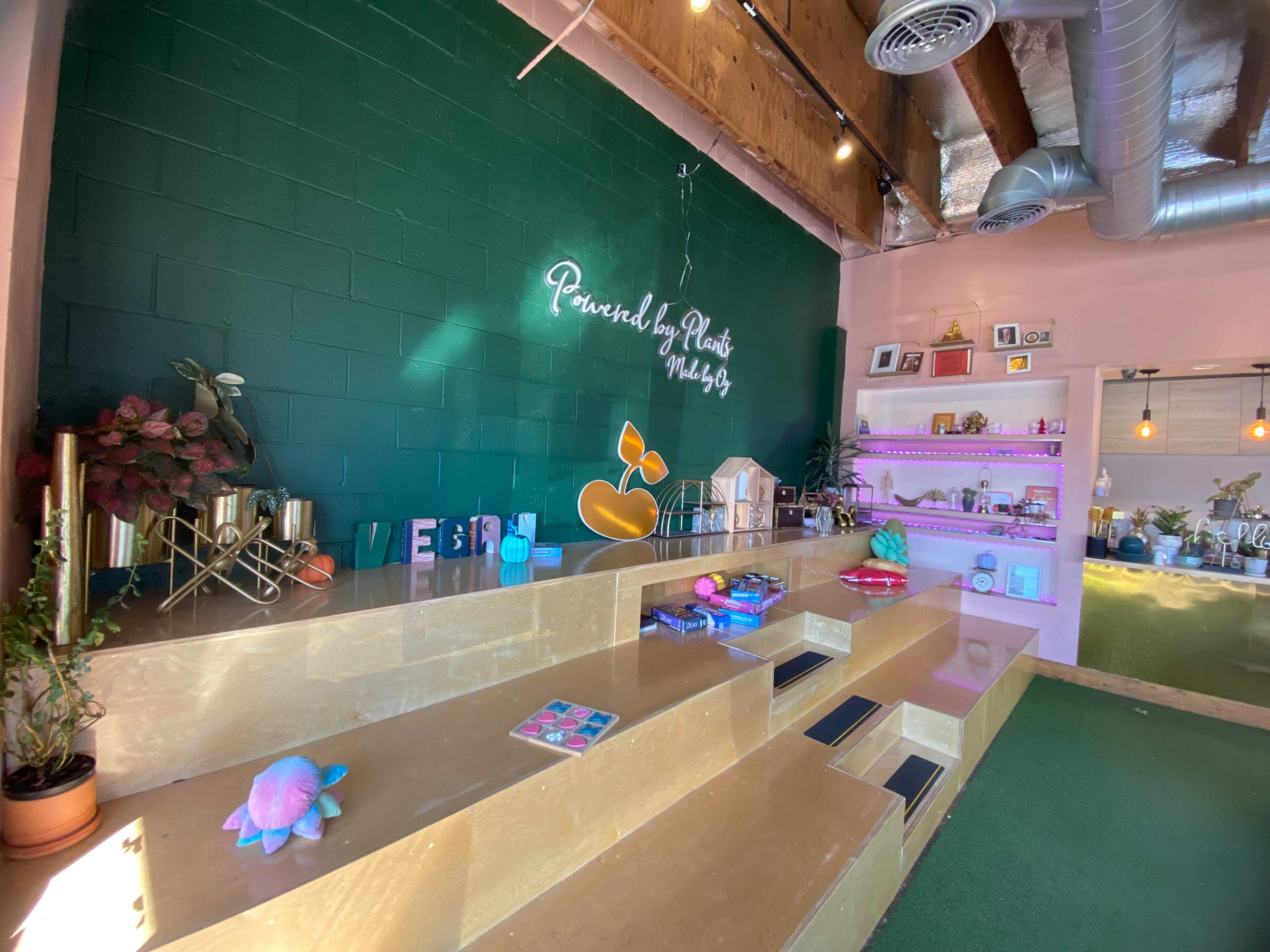 The interior features a green accent wall with decorative items on golden stairs, illuminated shelves, and a neon sign.