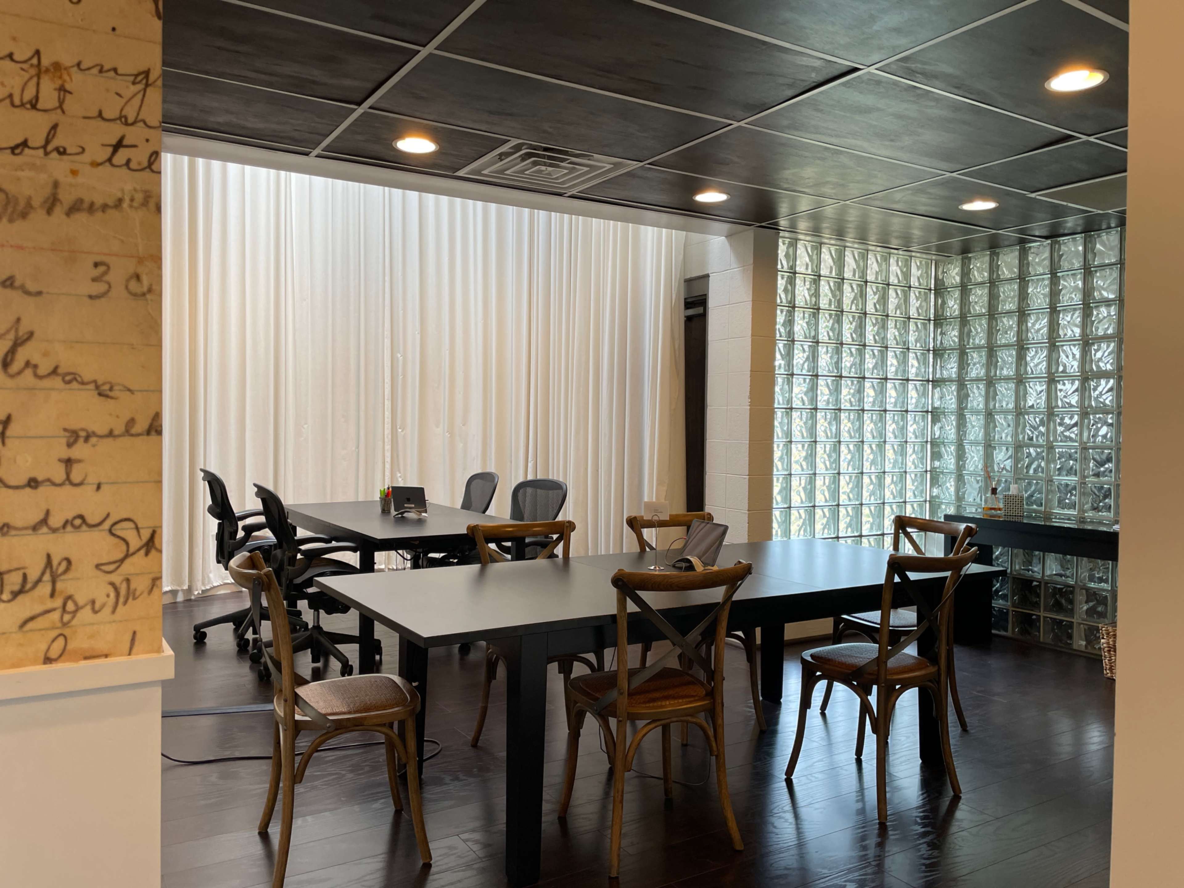 The image shows a modern conference room with a large table, several chairs, and a wall made of glass blocks, illuminated by overhead lights.