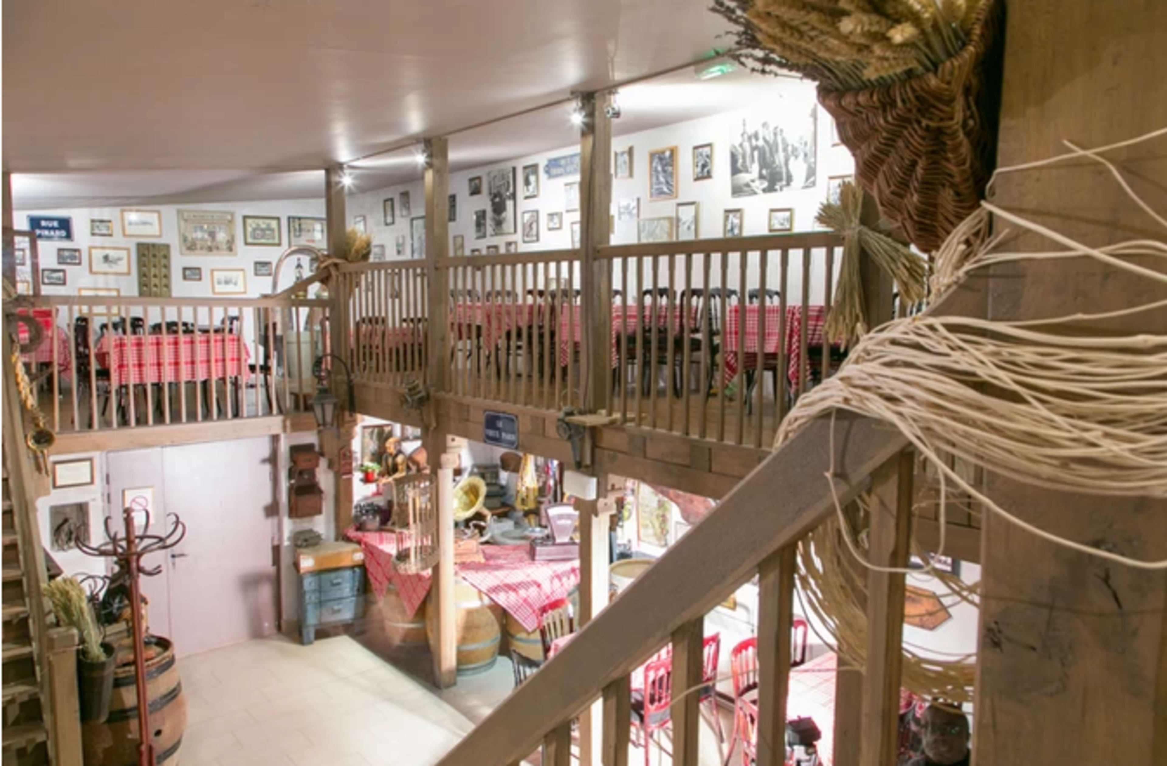 A two-story dining area with wooden railings and tables covered with red checkered tablecloths, adorned with various framed pictures on the walls.