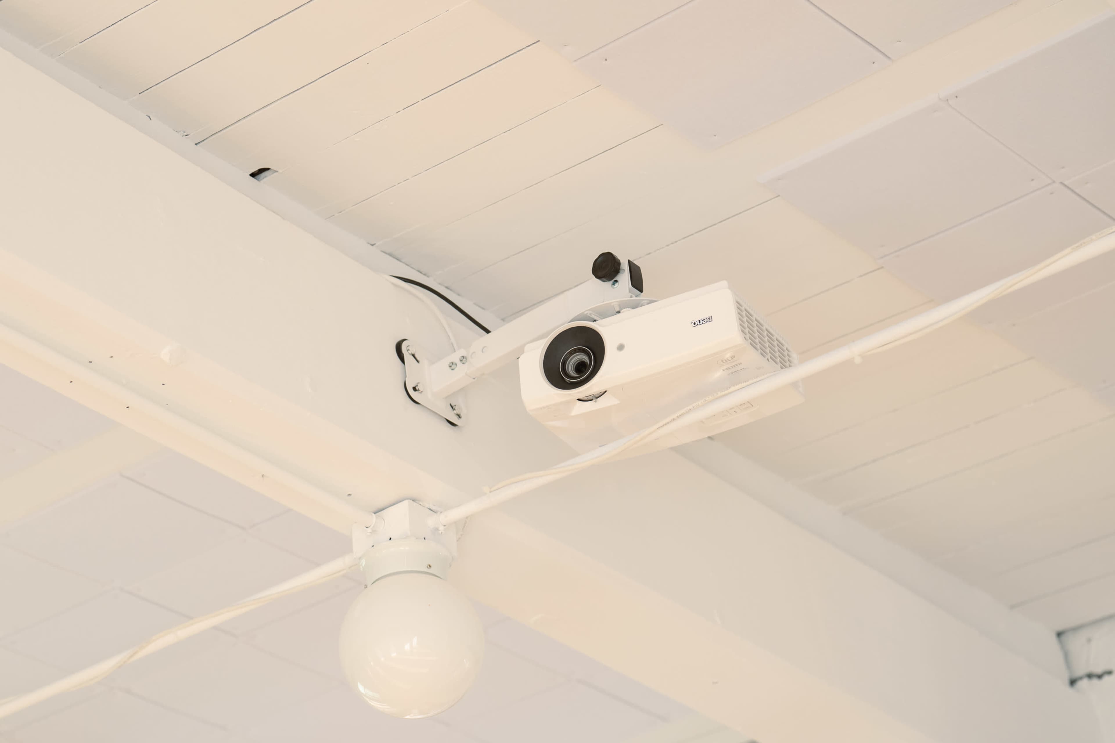 A projector is mounted on the ceiling with a white bulb hanging nearby.