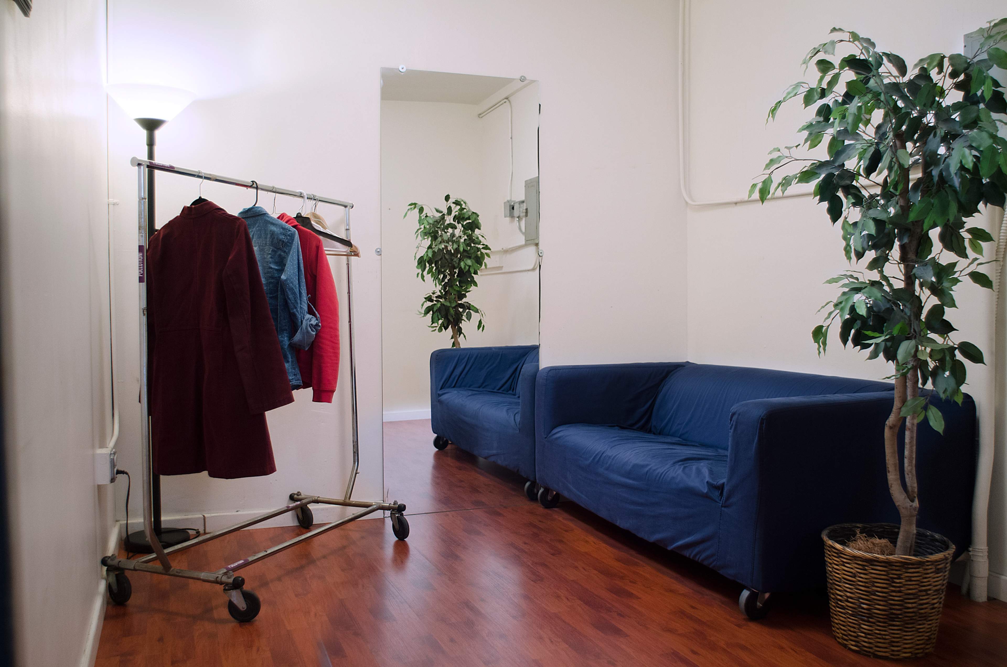 A clothing rack with garments hangs in a hallway beside two blue sofas and a potted plant.