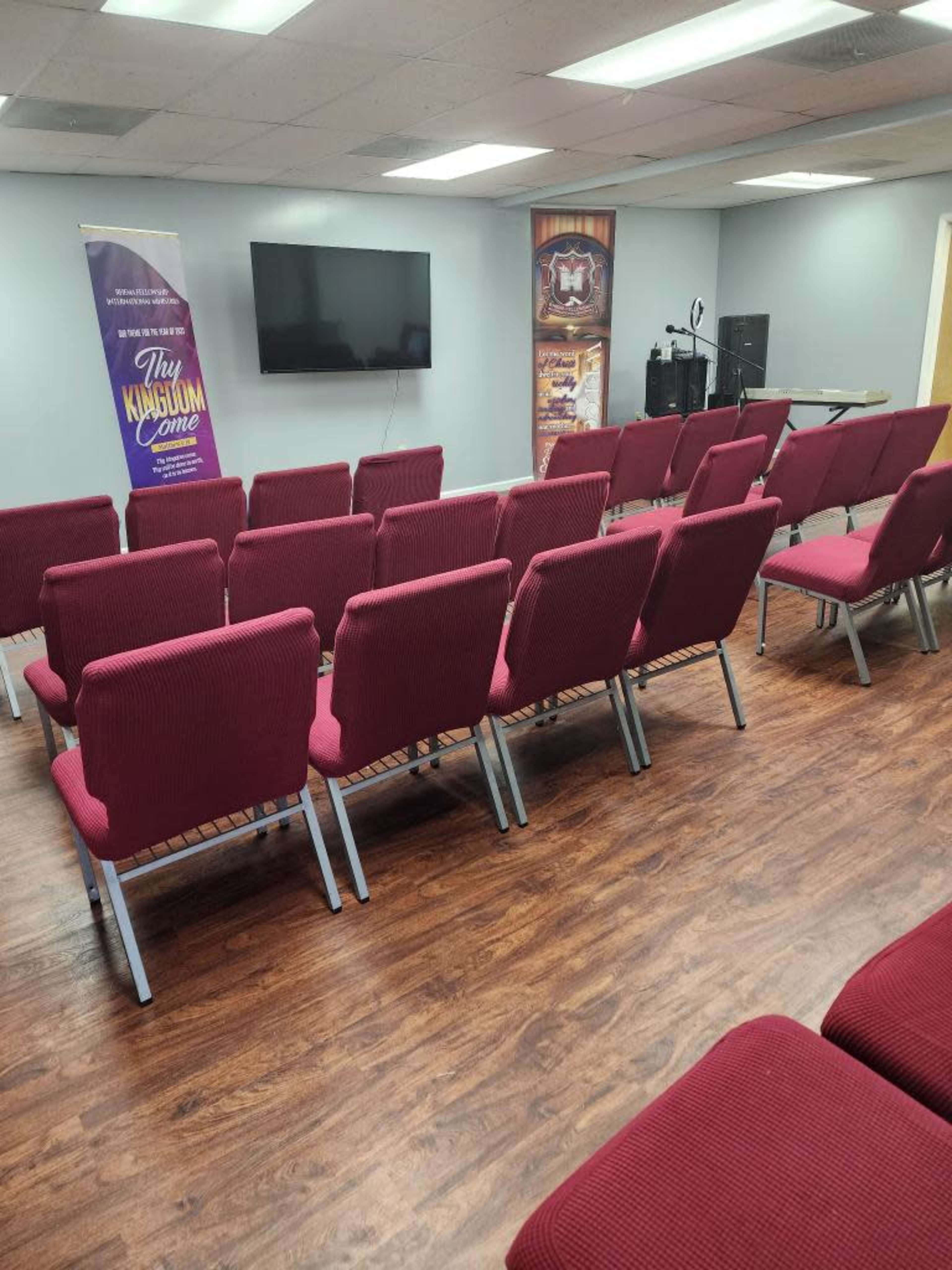 A meeting room with rows of maroon chairs facing a wall-mounted television and a podium.
