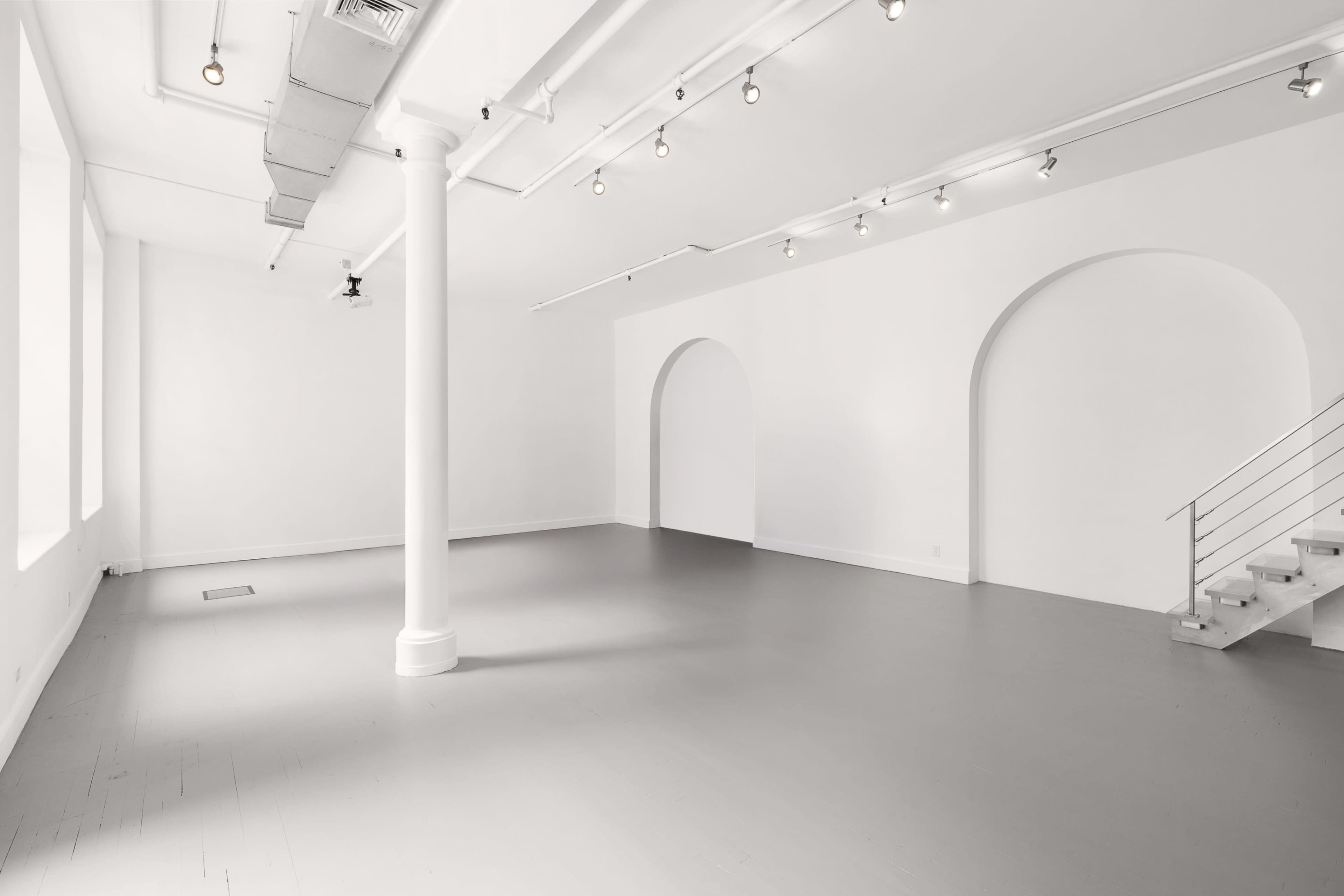 The image shows a spacious, bright room with white walls and a polished gray floor, featuring a column and arched openings leading to other areas.