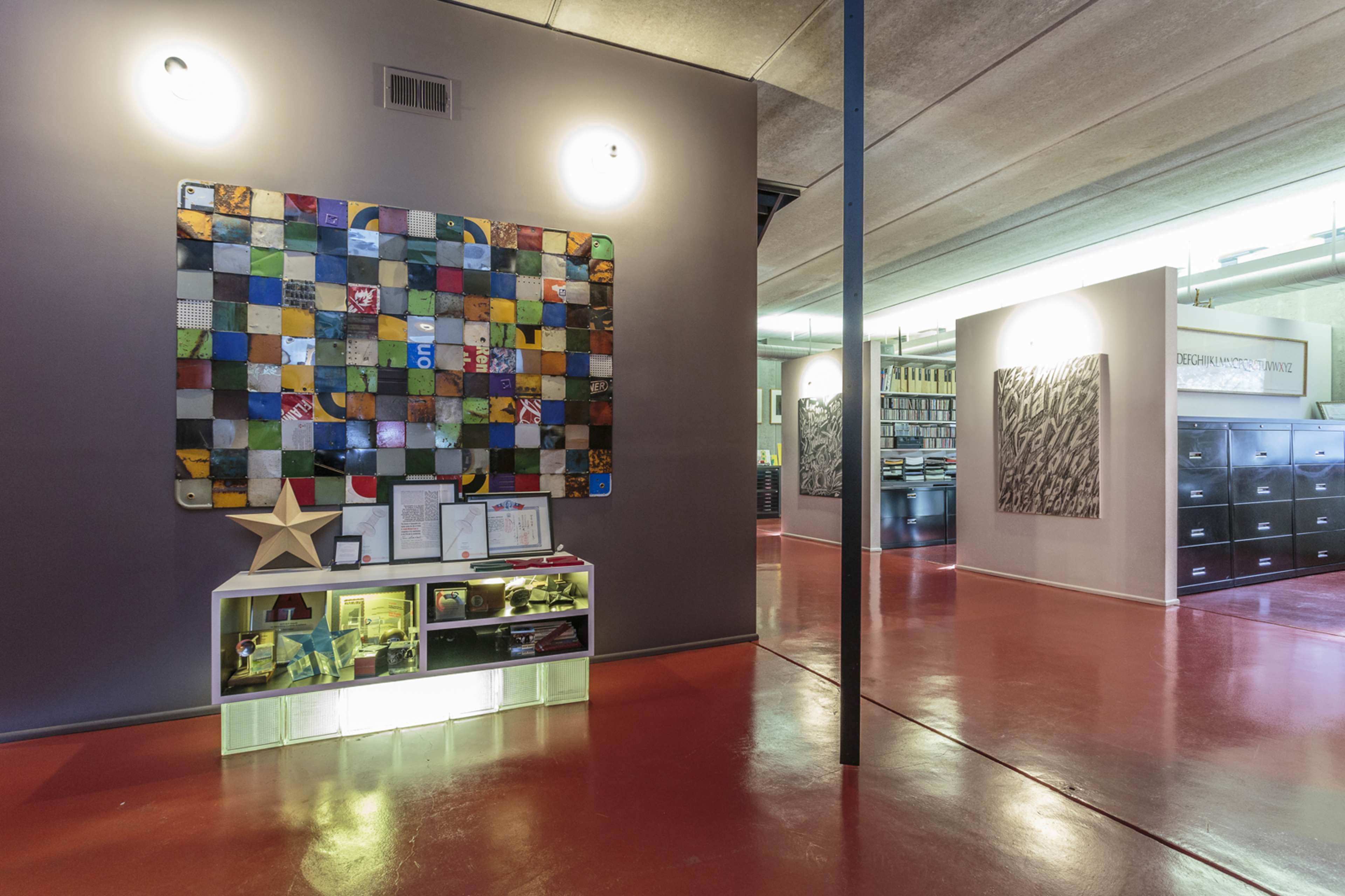 A modern interior of a room featuring a colorful wall artwork, a display cabinet with various items, and bookshelves in the background.