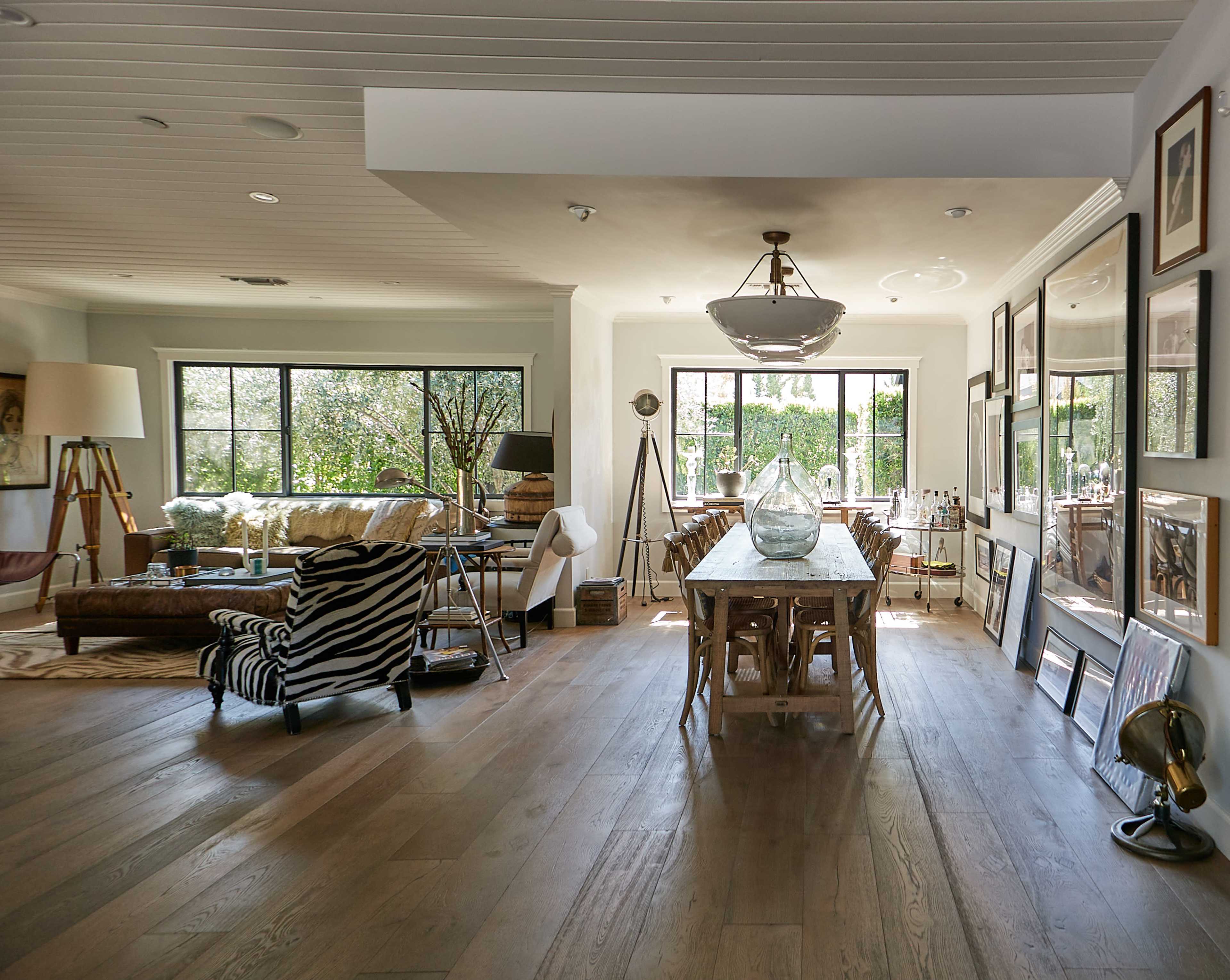 The image shows a spacious, modern living area featuring a dining table, a zebra-print chair, and large windows overlooking a garden.