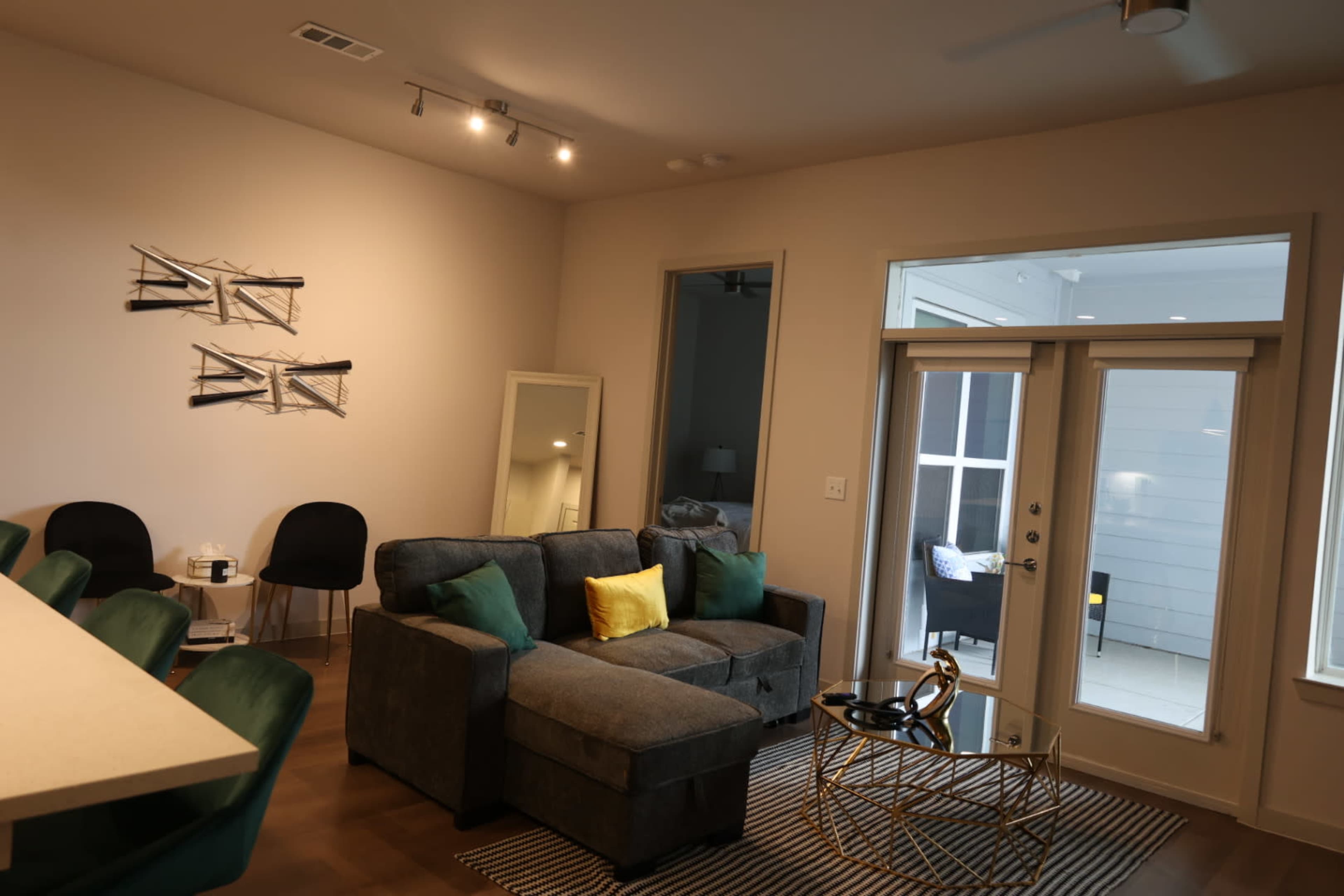A modern living room features a gray sectional sofa with green and yellow pillows, a round coffee table, and large doors leading to an outdoor space.