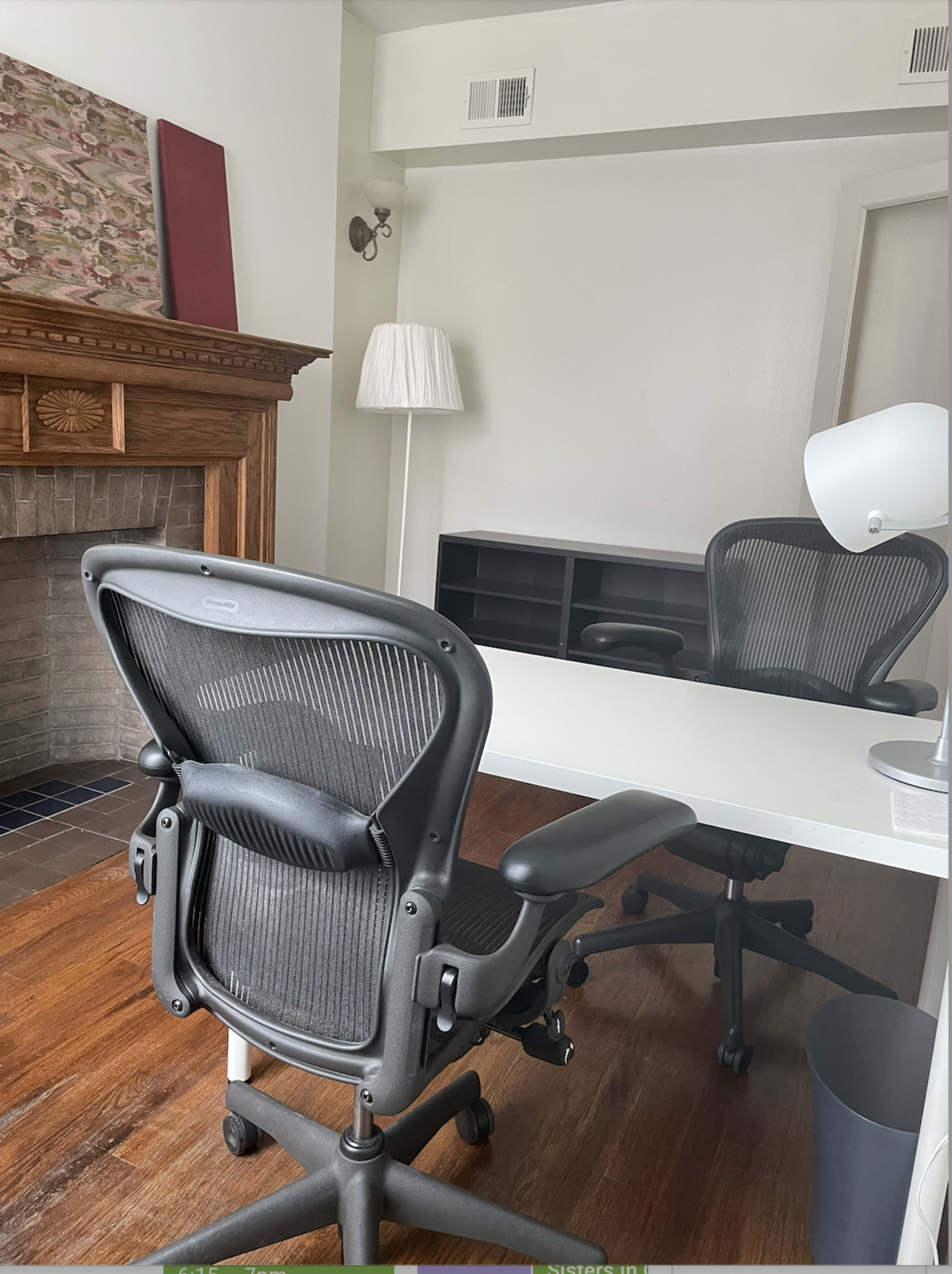 A modern office space features a sleek desk, an ergonomic chair, a lamp, and a wooden fireplace with decorative elements.