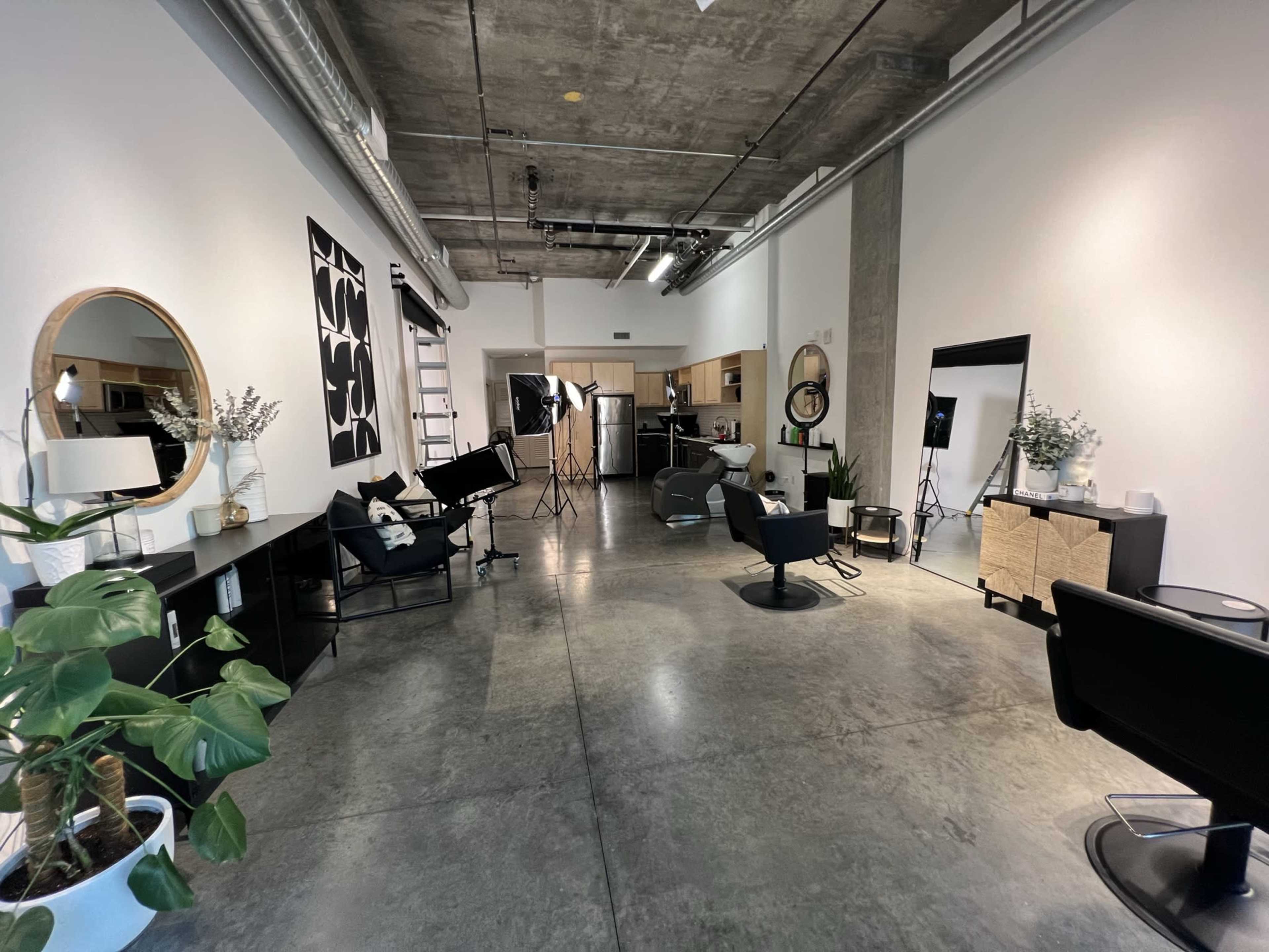 The image shows a modern hair salon with sleek furnishings, a concrete floor, and well-arranged workstations.