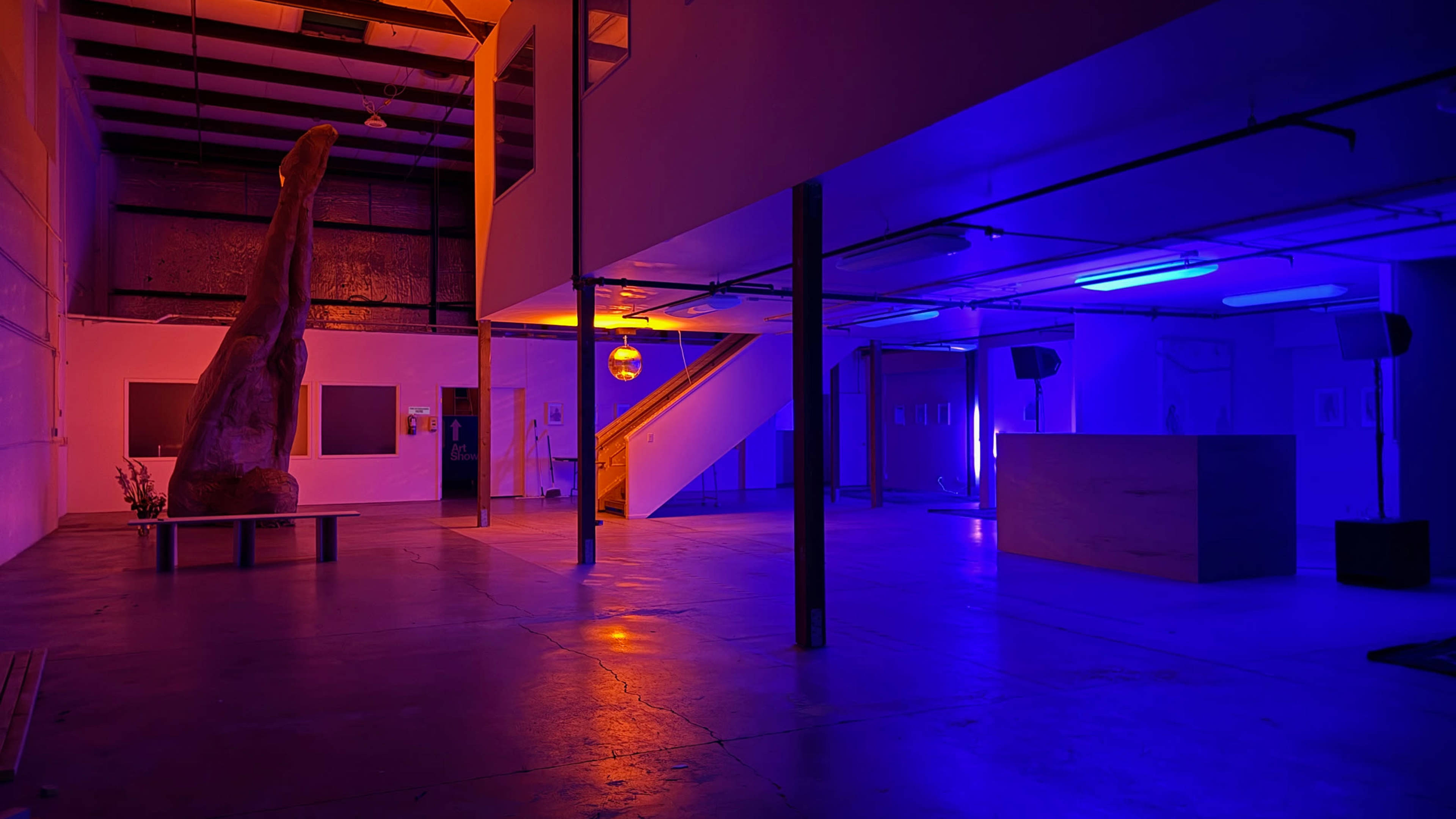 The image shows an industrial-style interior space with a staircase, featuring vibrant blue and orange lighting.