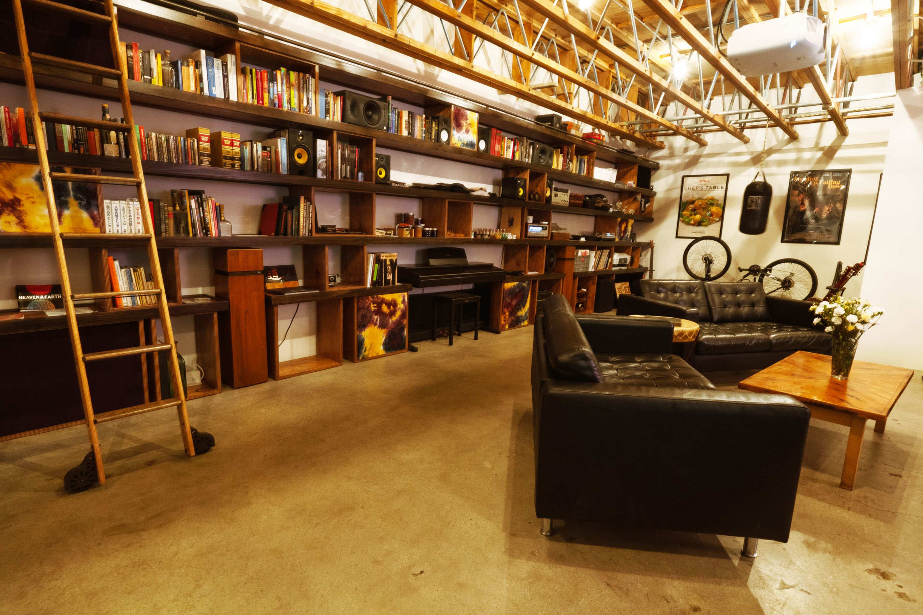 A modern interior space with a black leather couch, a wooden coffee table, bookshelves filled with books, and a ladder leaning against the shelves.