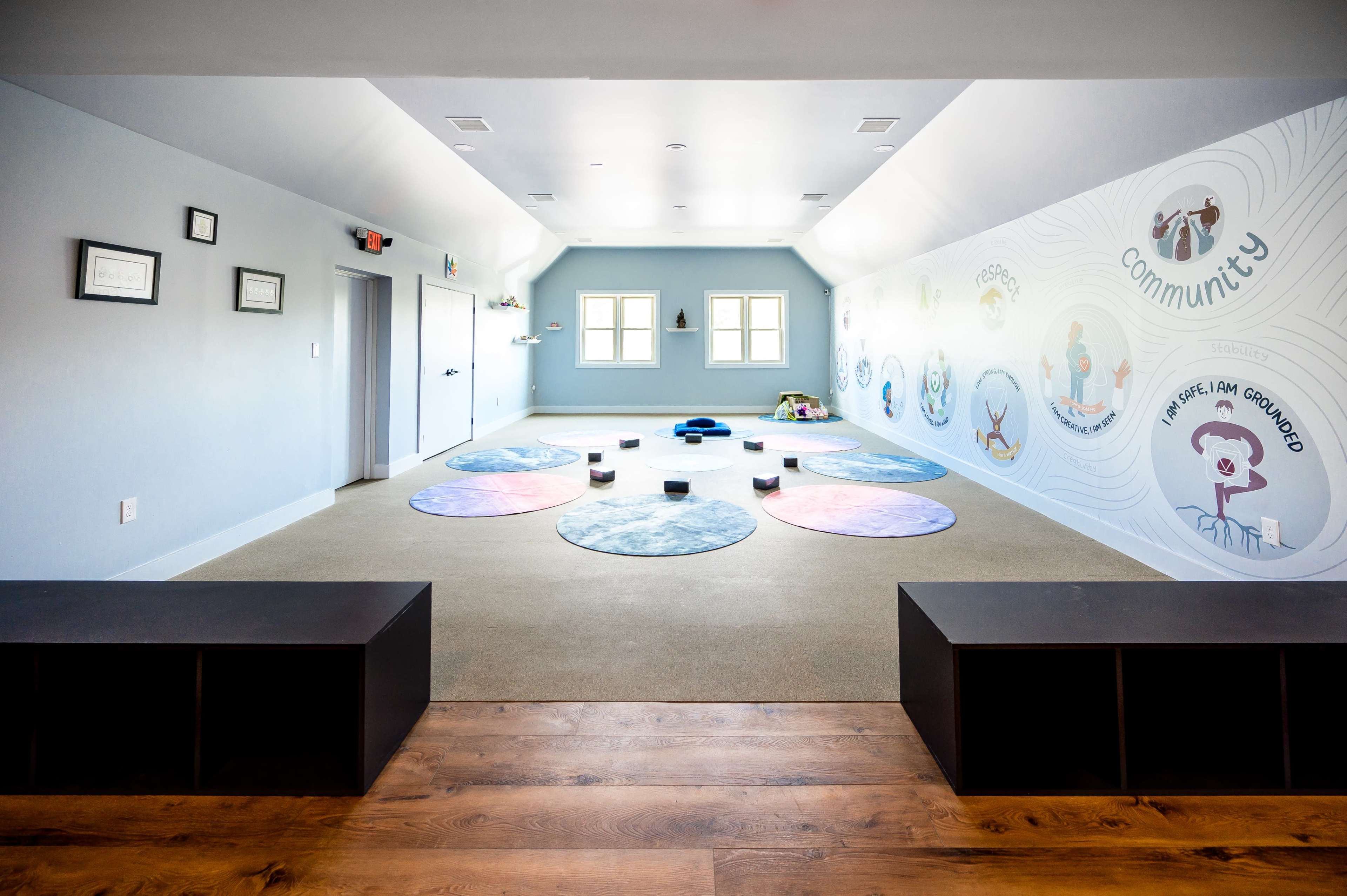 A spacious, carpeted room designed for activities, featuring colorful circular mats arranged on the floor and a mural on one wall.