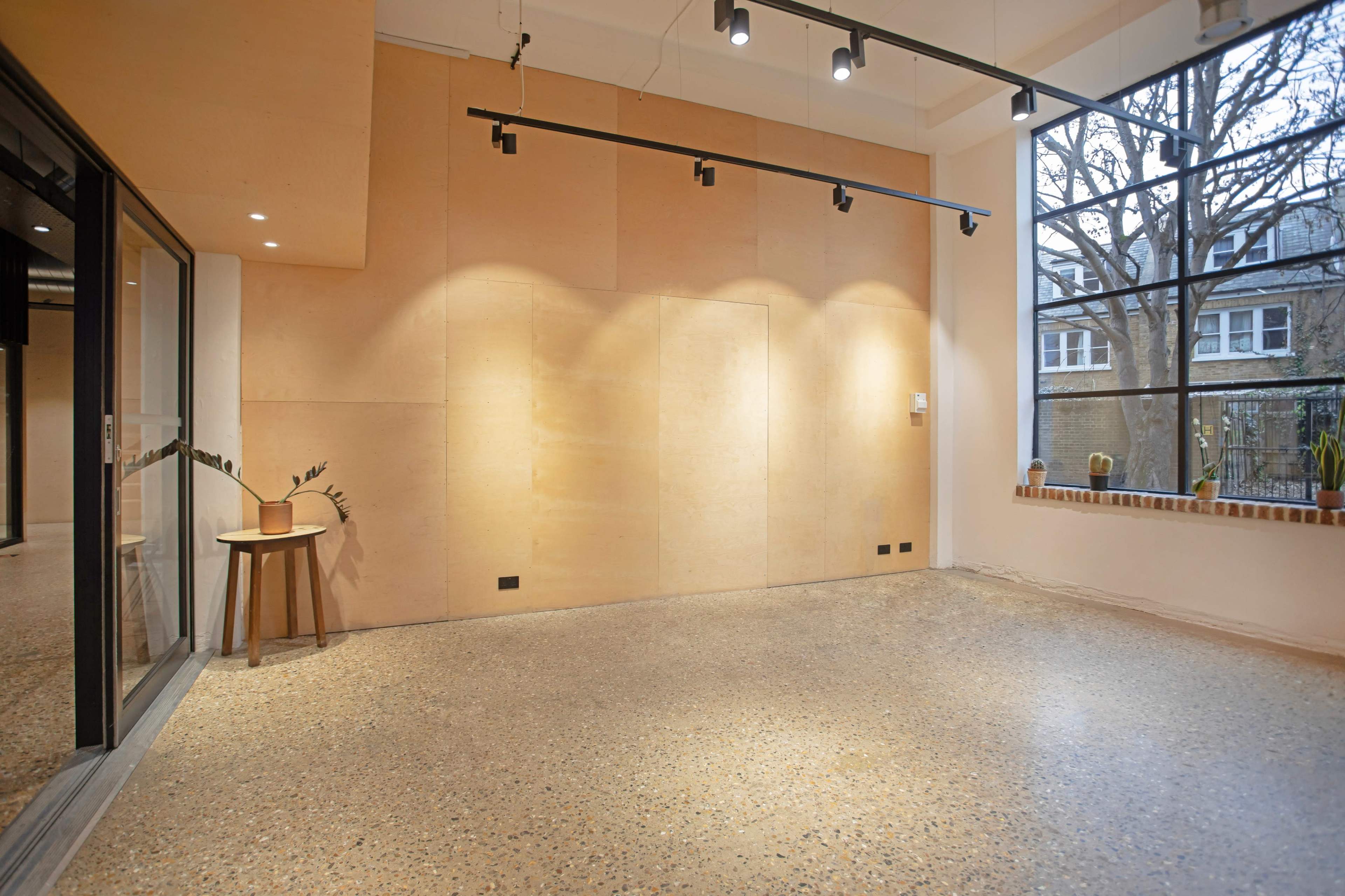 A minimalist interior space with a smooth, light-colored concrete floor, wooden paneling on the walls, and large windows overlooking a garden.