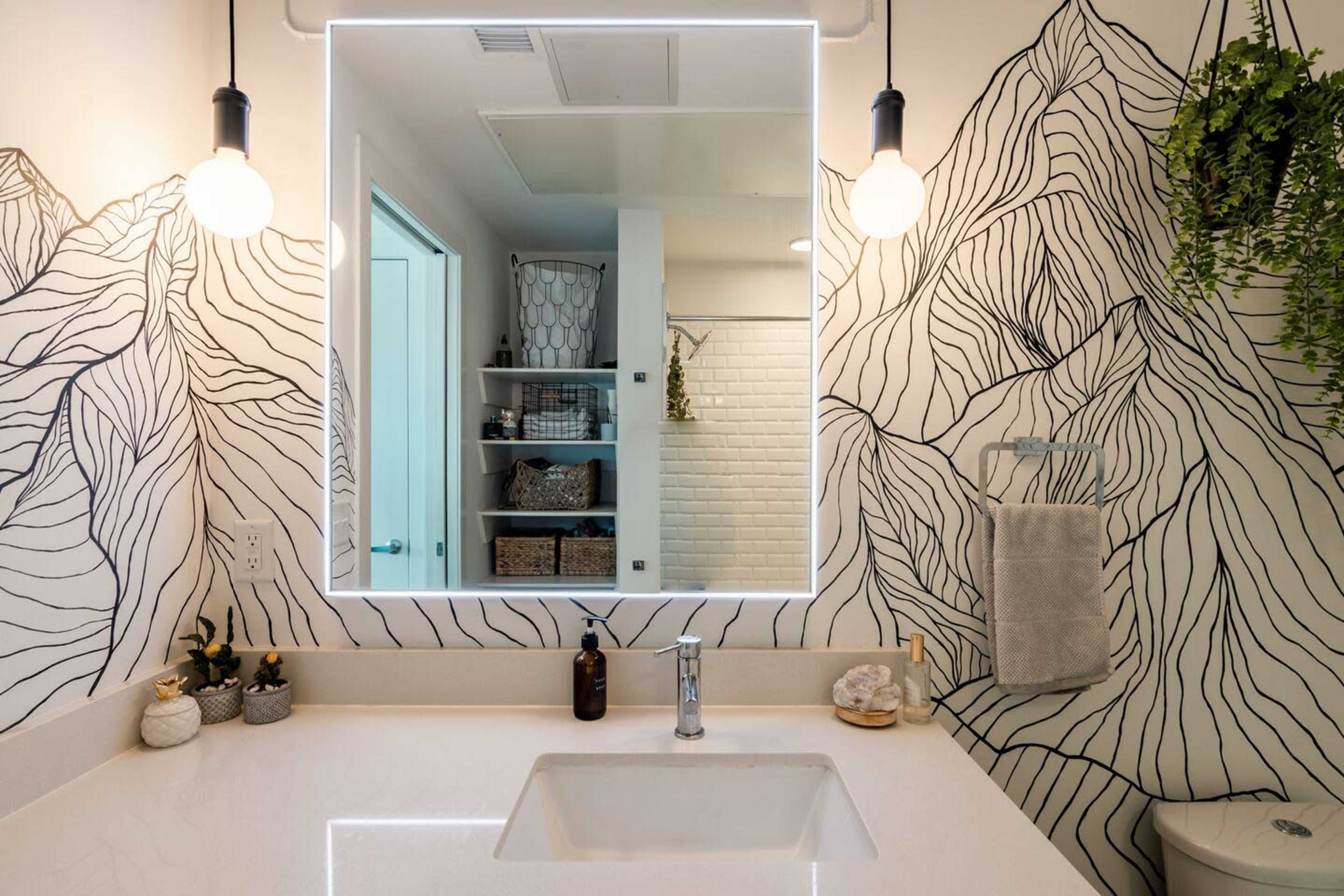 A bathroom features a mountain-themed mural, a large illuminated mirror, and a modern sink with minimalistic decor.