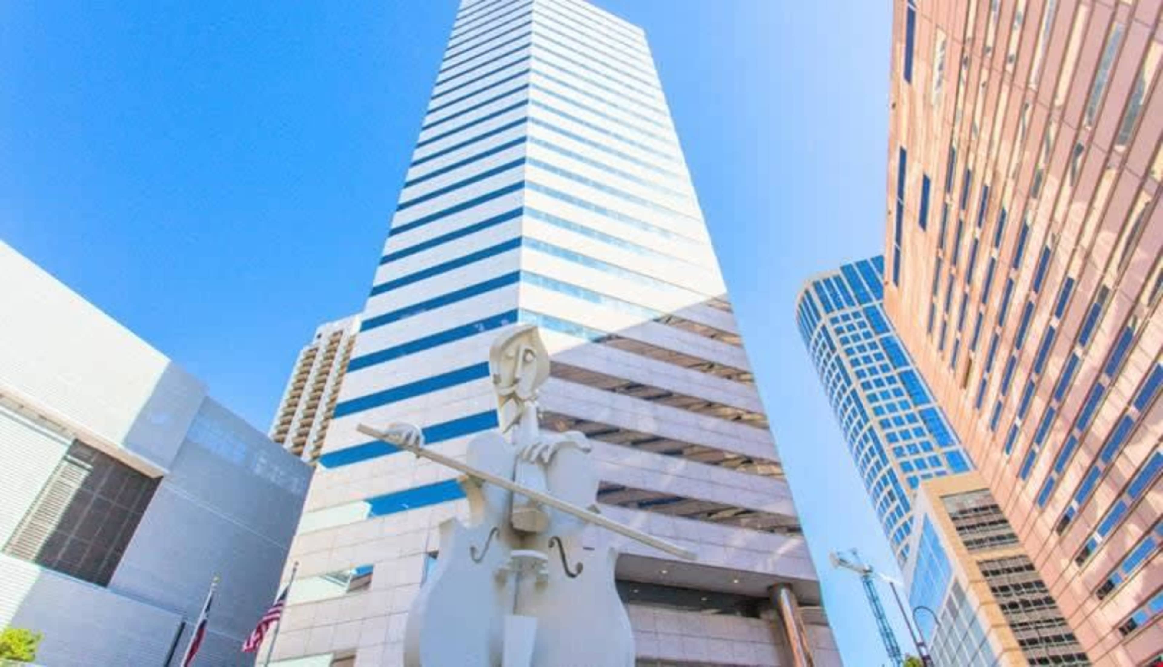 A large white sculpture of a figure with a violin stands in front of a tall, multi-story building with a striped facade.