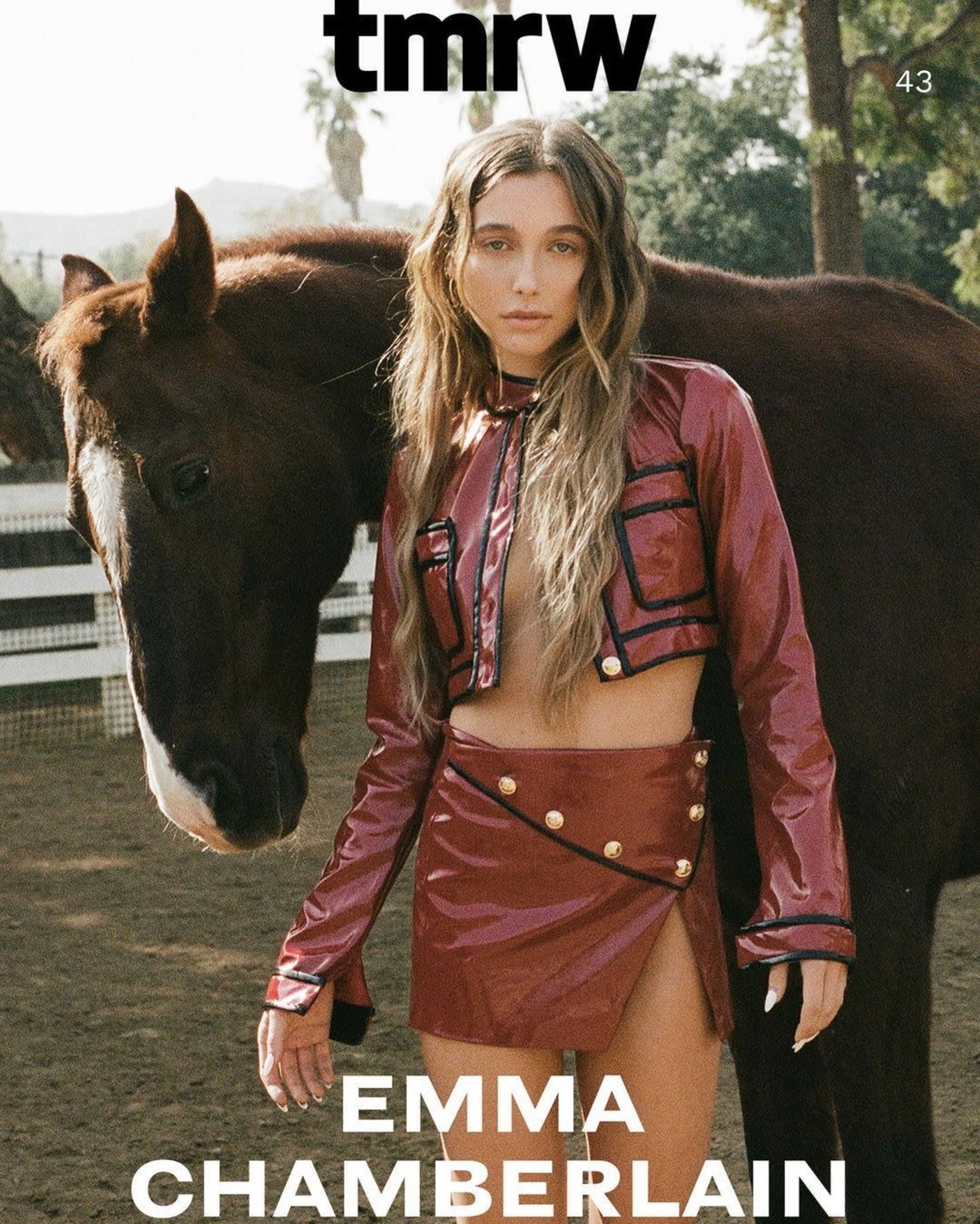 A person in a shiny red outfit poses next to a horse in a stable setting.
