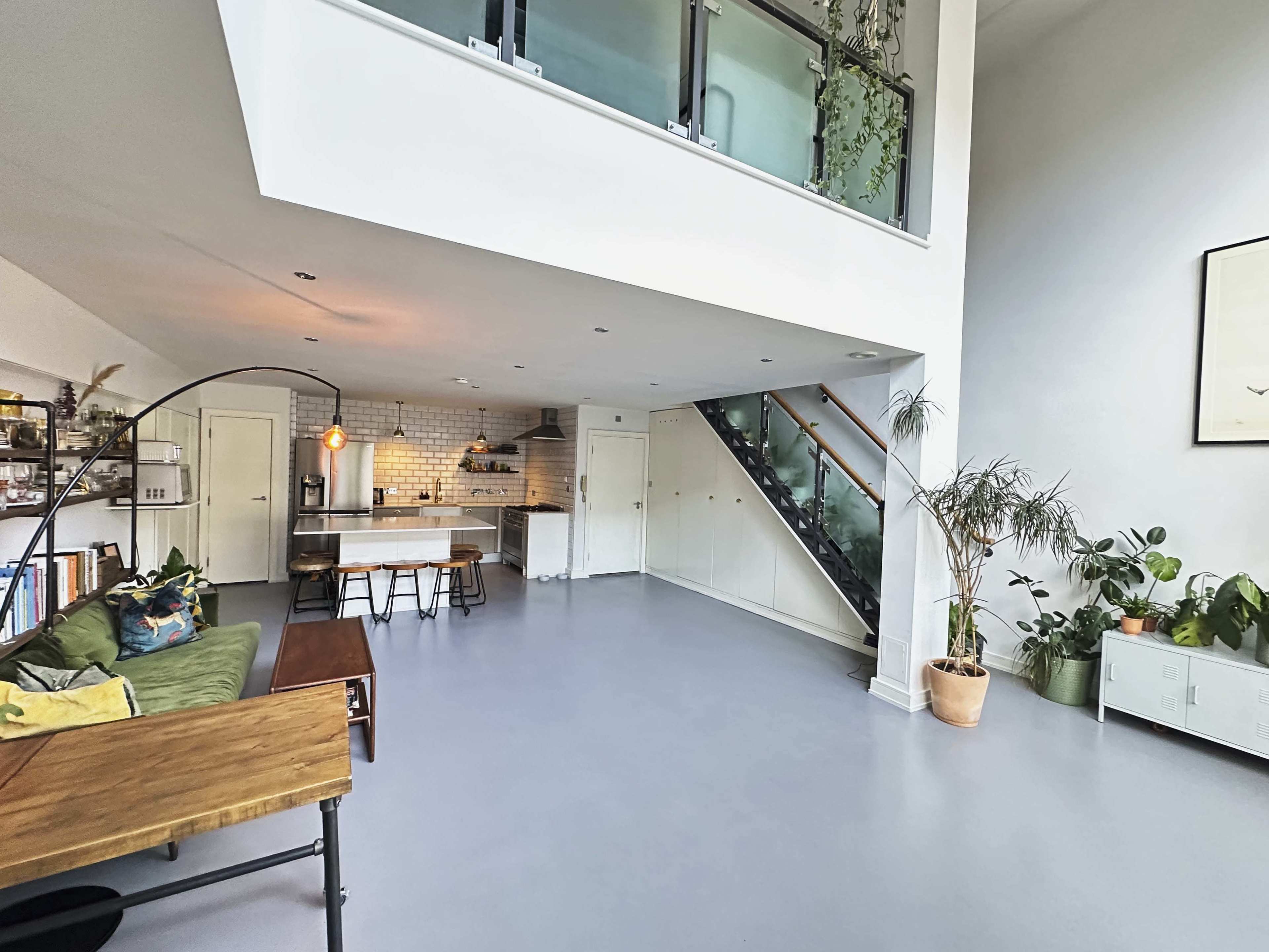 A spacious, modern living area with a kitchen, dining table, and staircase, featuring plants and minimalist decor.