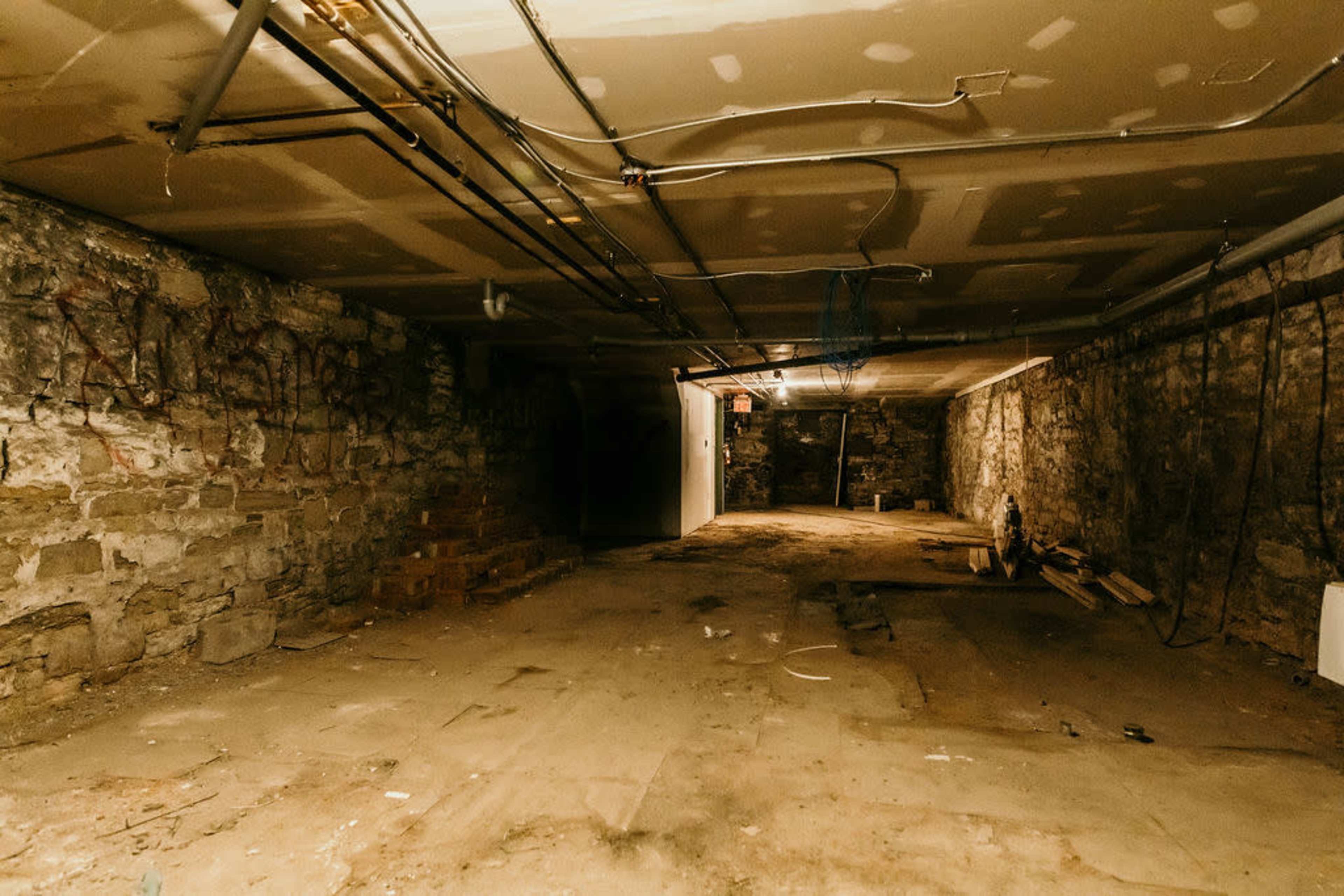 A spacious, unfinished basement with stone walls, exposed wiring, and a bare concrete floor.