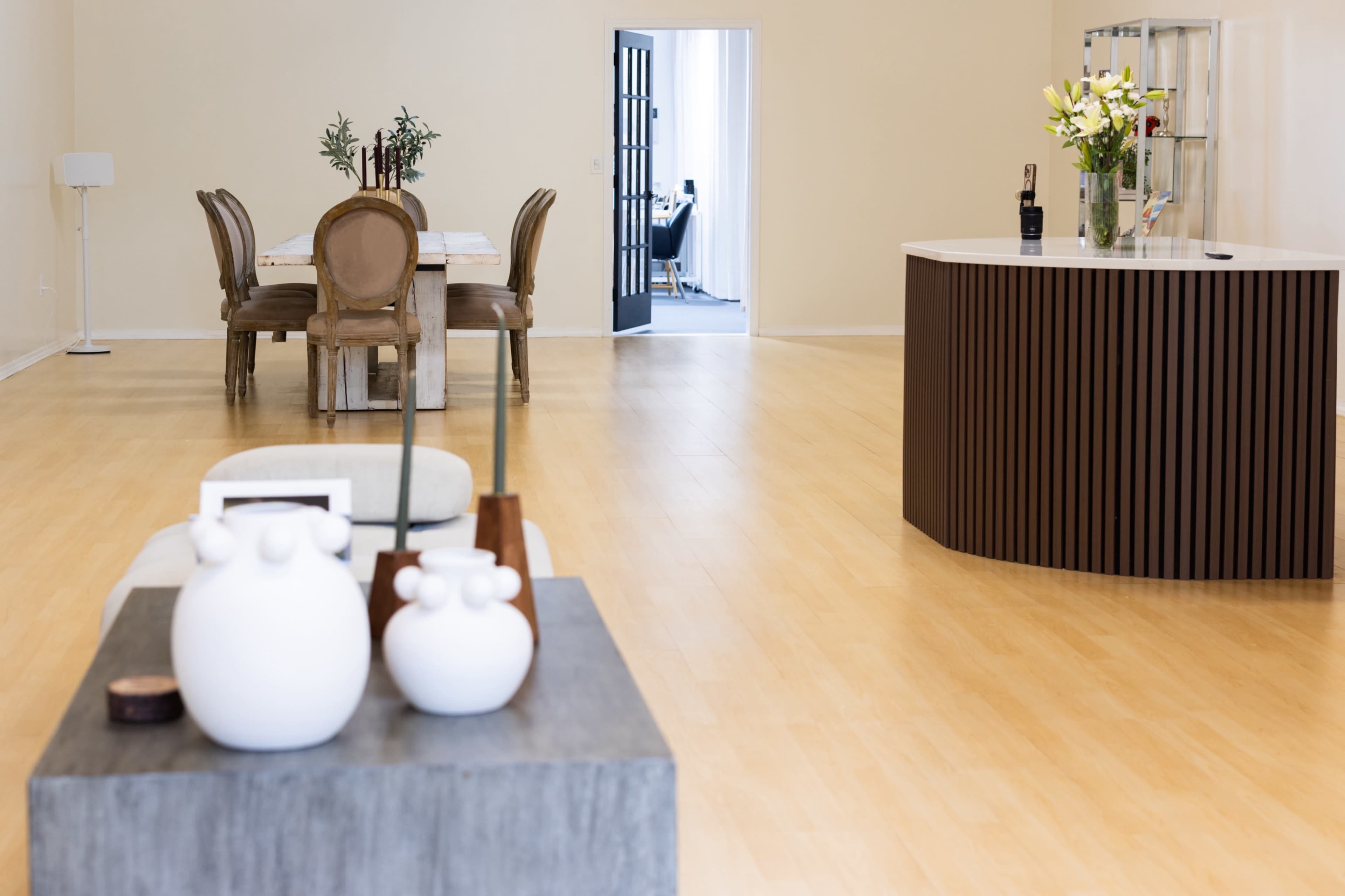 The image shows a spacious interior with a dining table set for six, a minimalist coffee table in the foreground, and a reception area featuring a curved counter.
