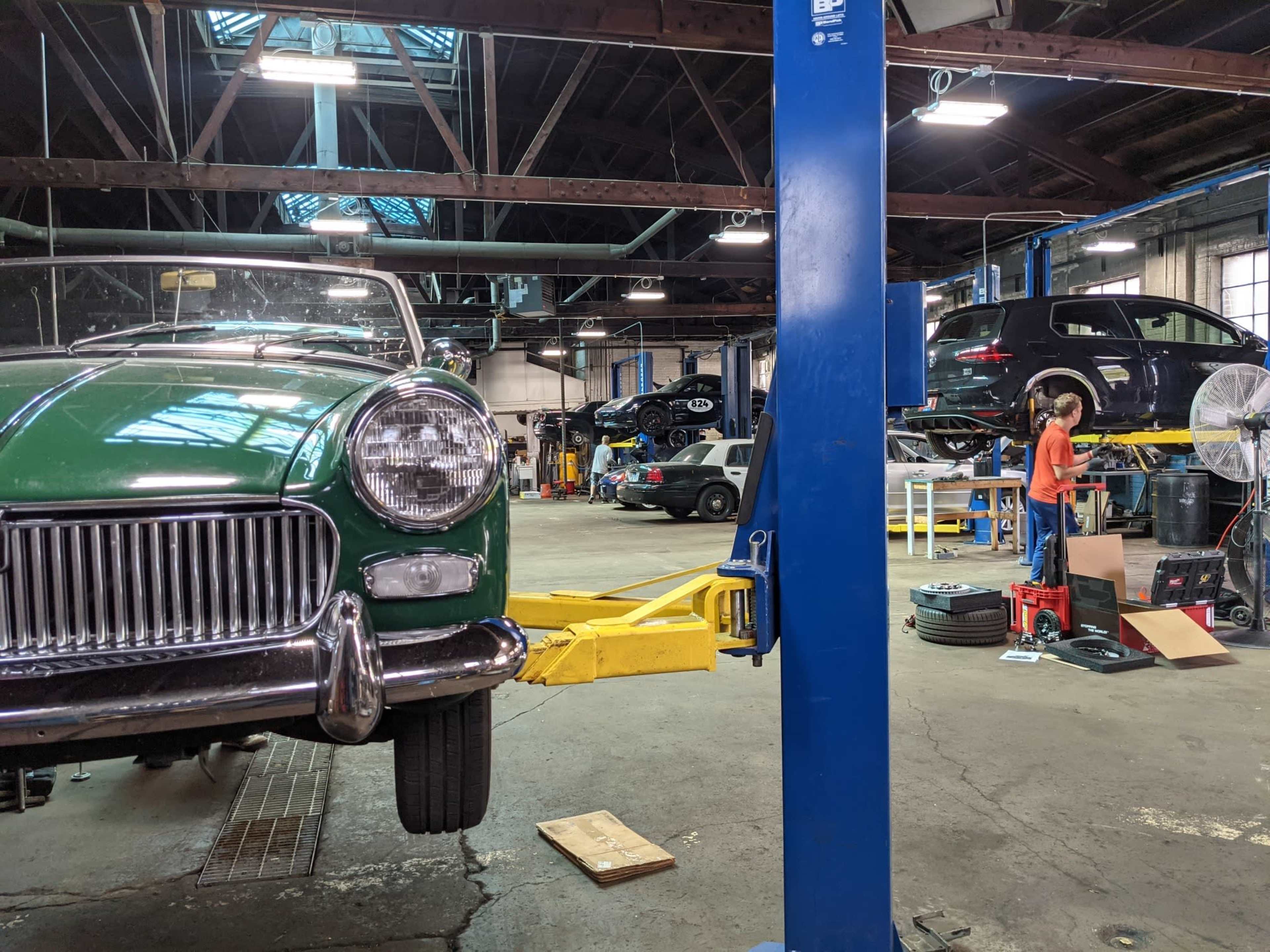 A car repair shop with a vintage green car on a lift and several vehicles being worked on in the background.