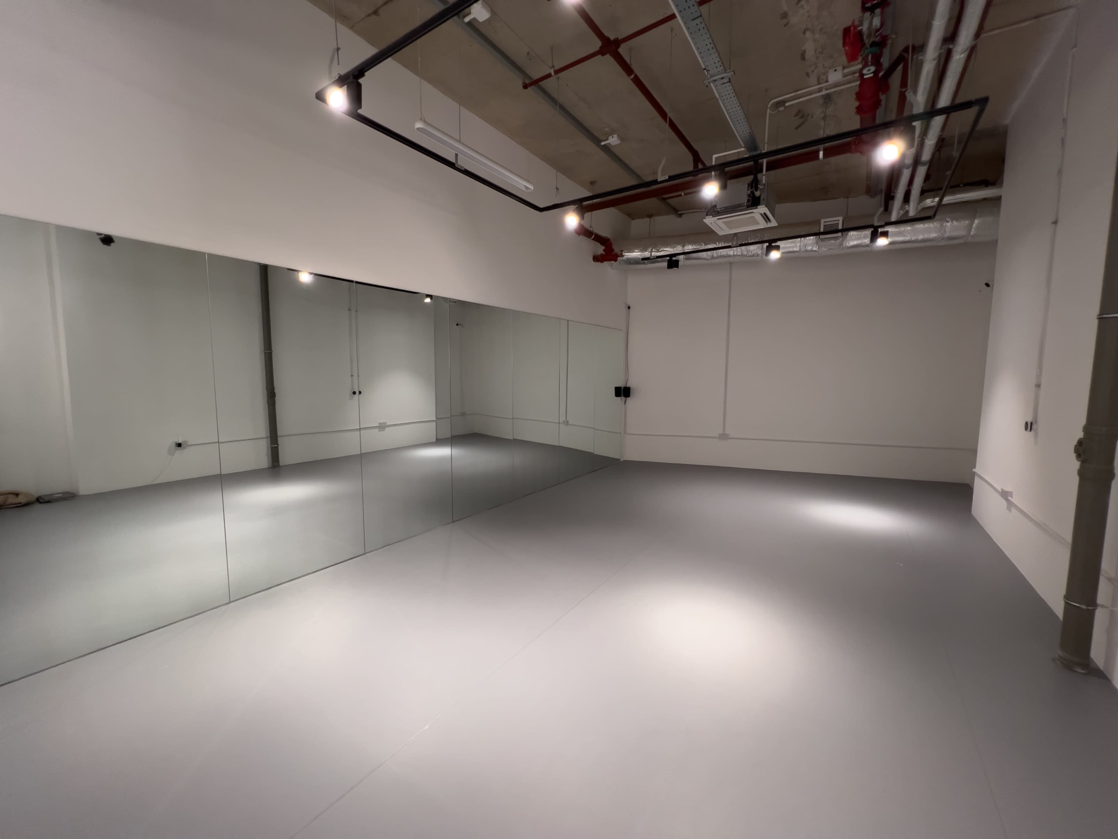 The image shows an empty studio space with gray flooring and a large mirror wall.