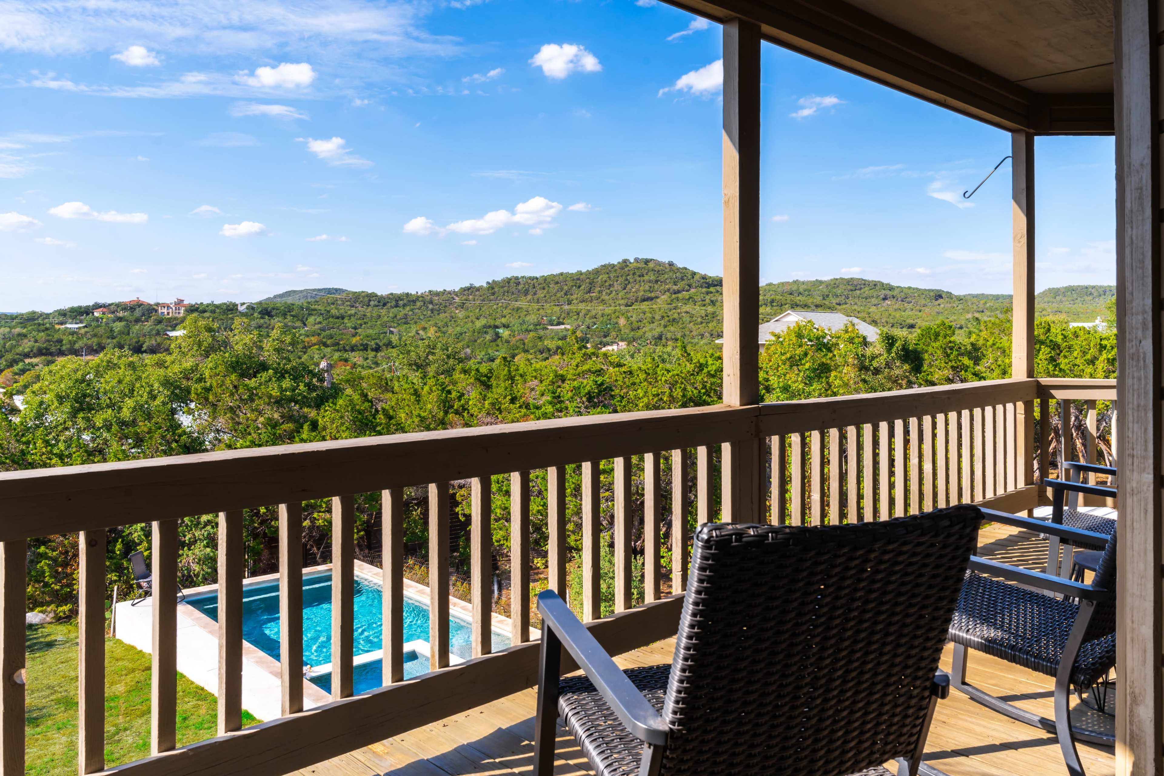 The image shows a wooden balcony overlooking a green landscape with a pool visible below.