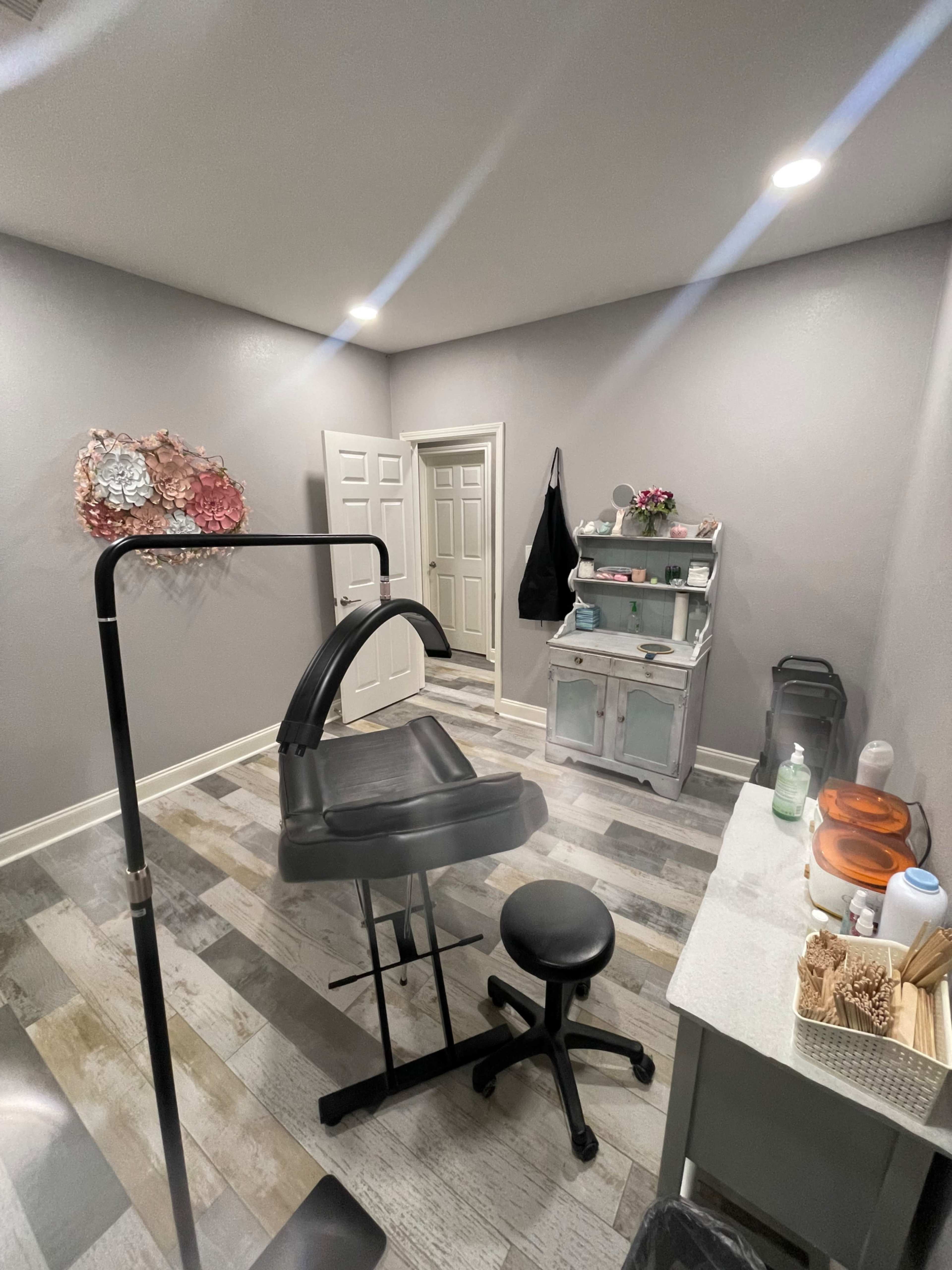 A small, well-lit treatment room with a black exam chair, a rolling stool, and a gray storage cabinet against the wall.