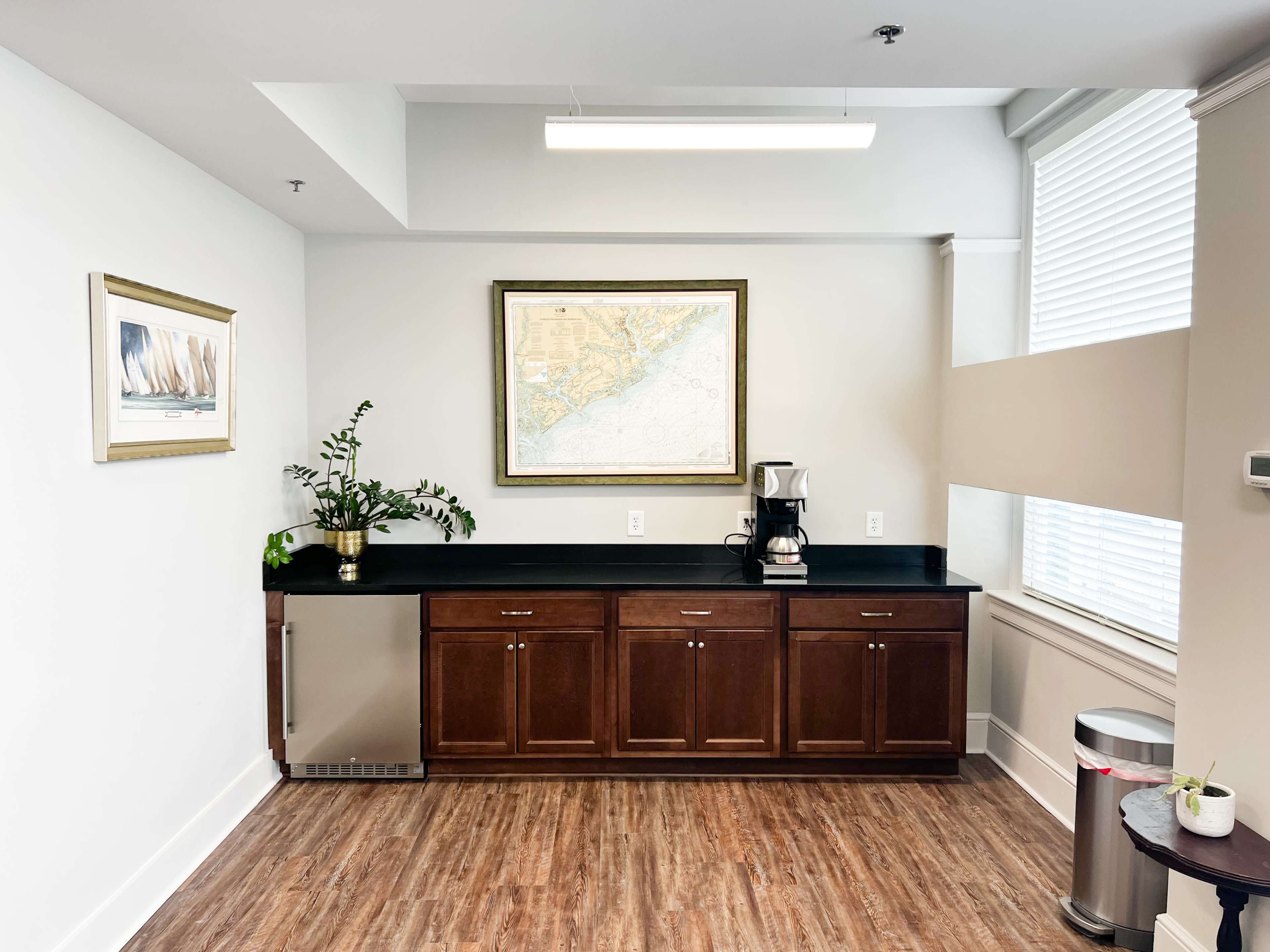 A kitchenette features dark cabinets under a wall-mounted map, with a coffee machine and a potted plant on the counter.