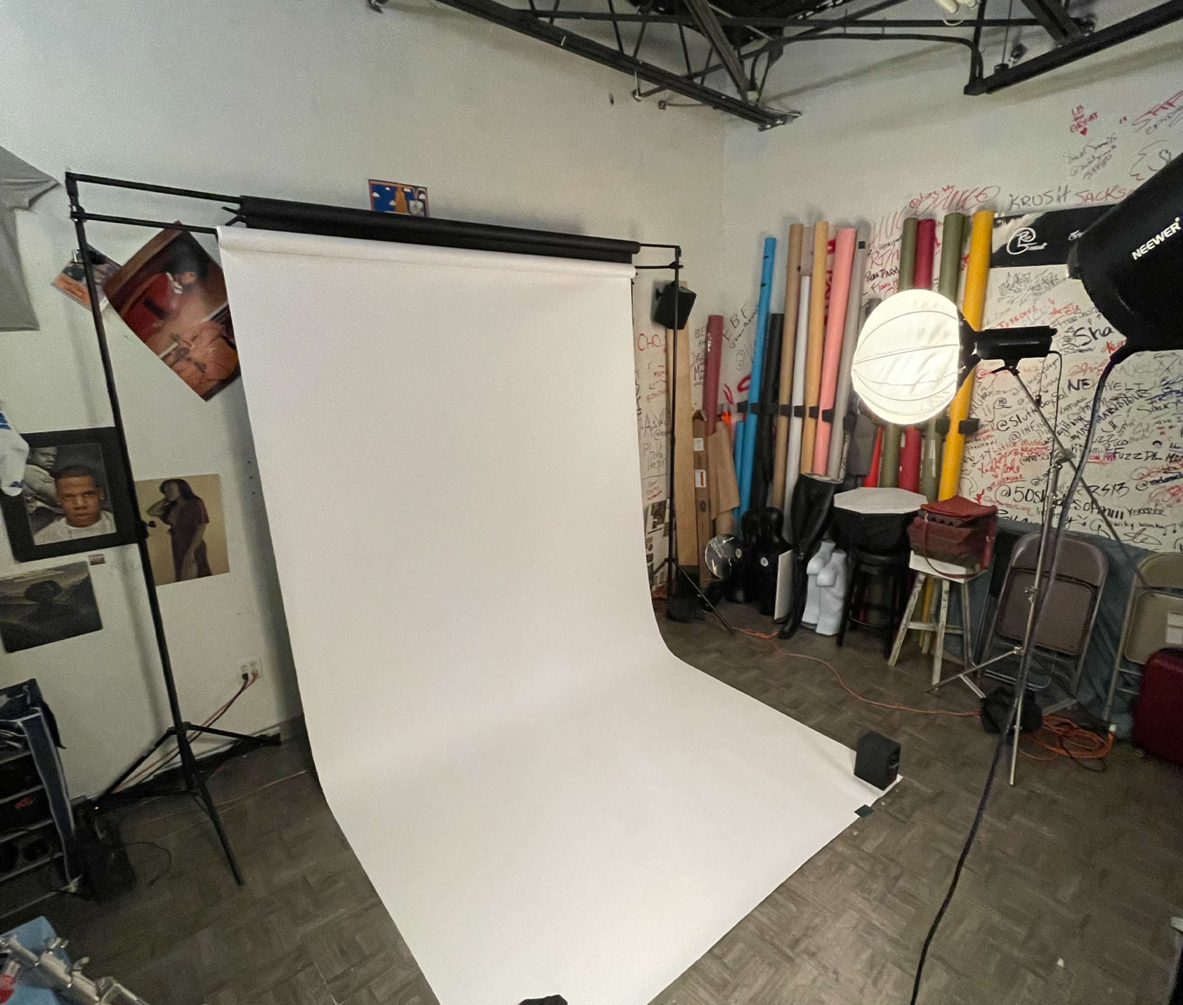 A photography studio setup with a white backdrop, lighting equipment, and various props and materials in the background.