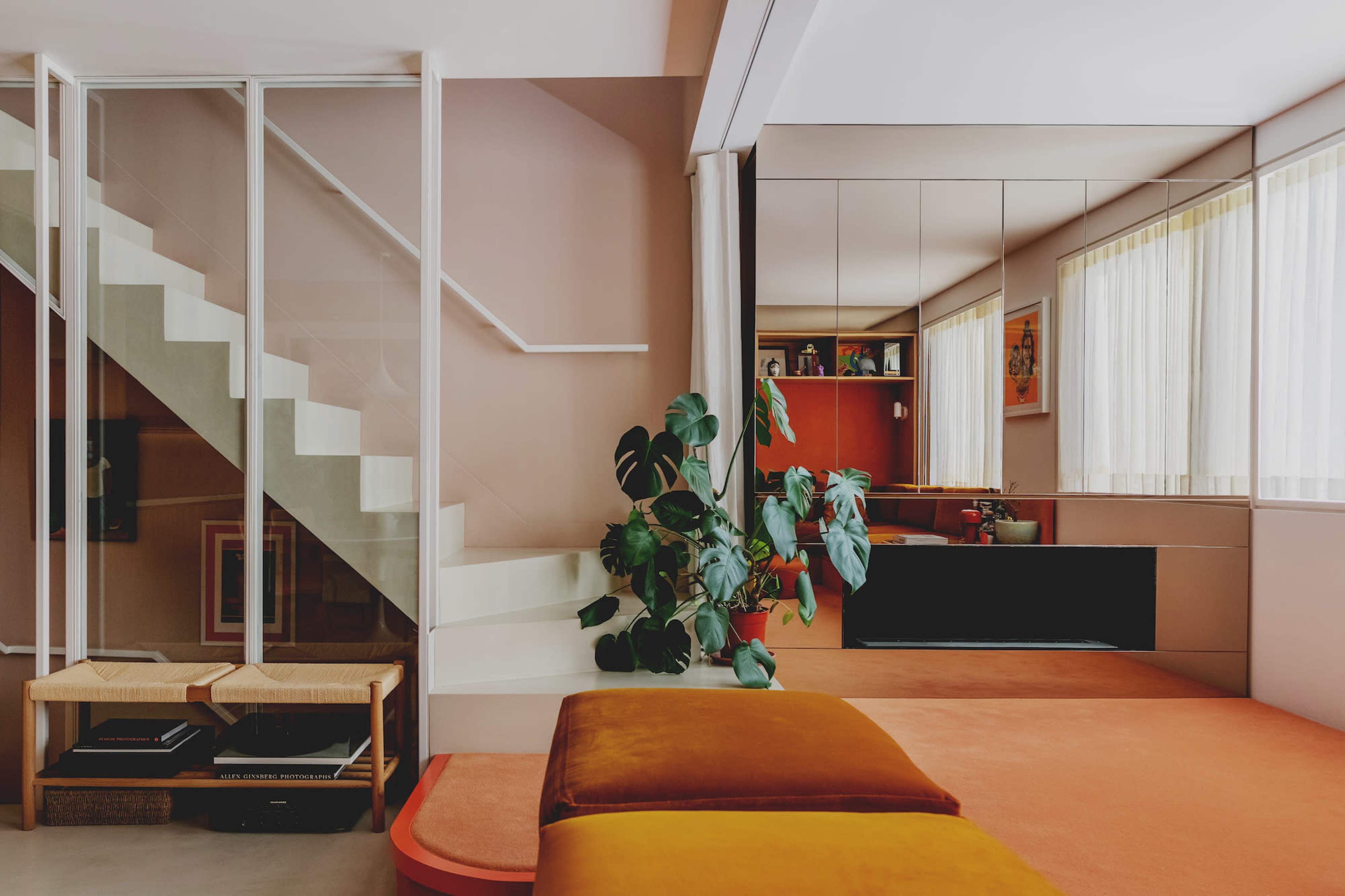 A modern living space featuring a staircase, a large mirror, a potted plant, and orange-colored flooring with a seating area.