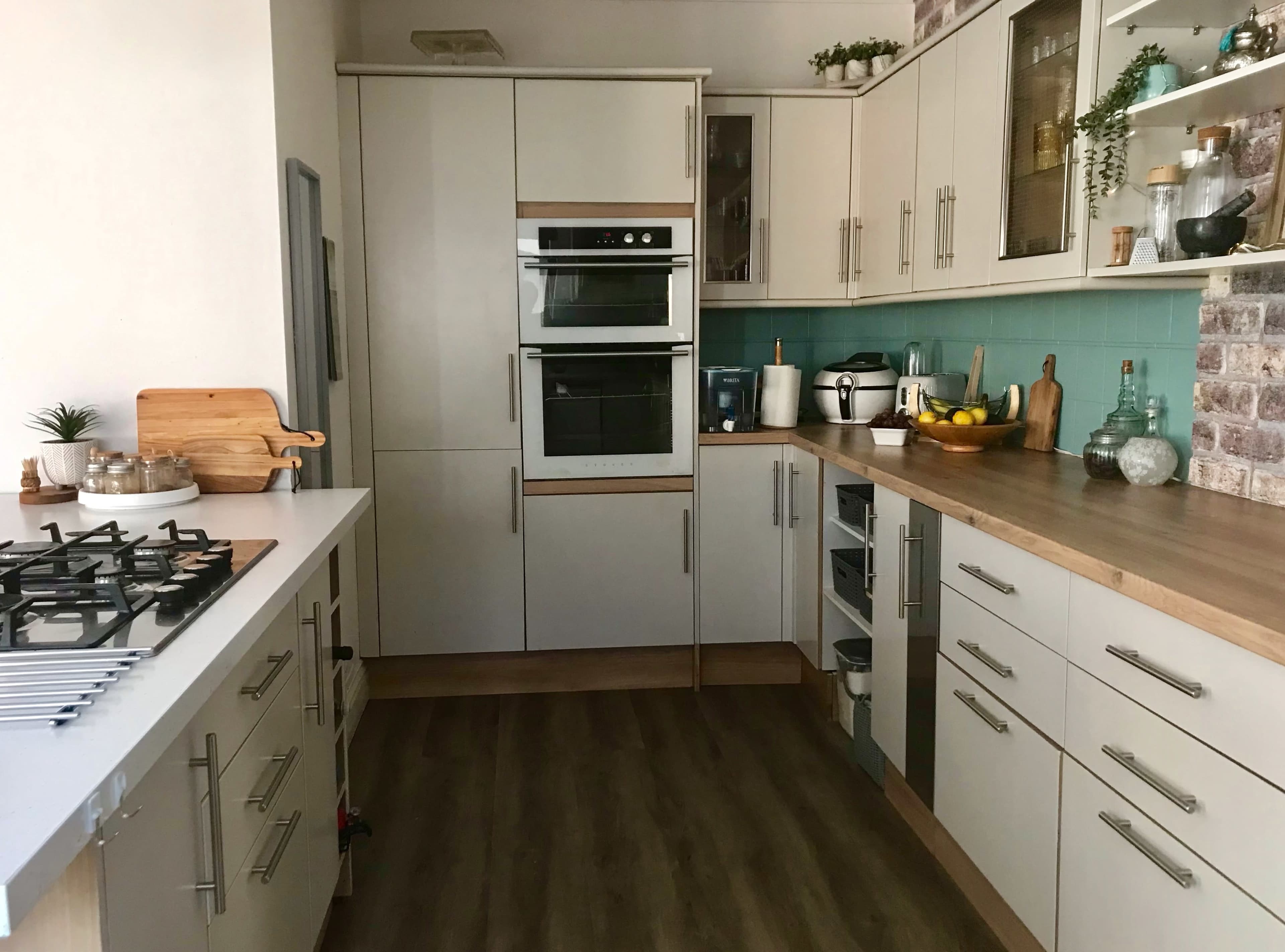 The kitchen features modern cabinetry, a built-in oven, a gas stove, and various appliances organized along a wooden countertop.