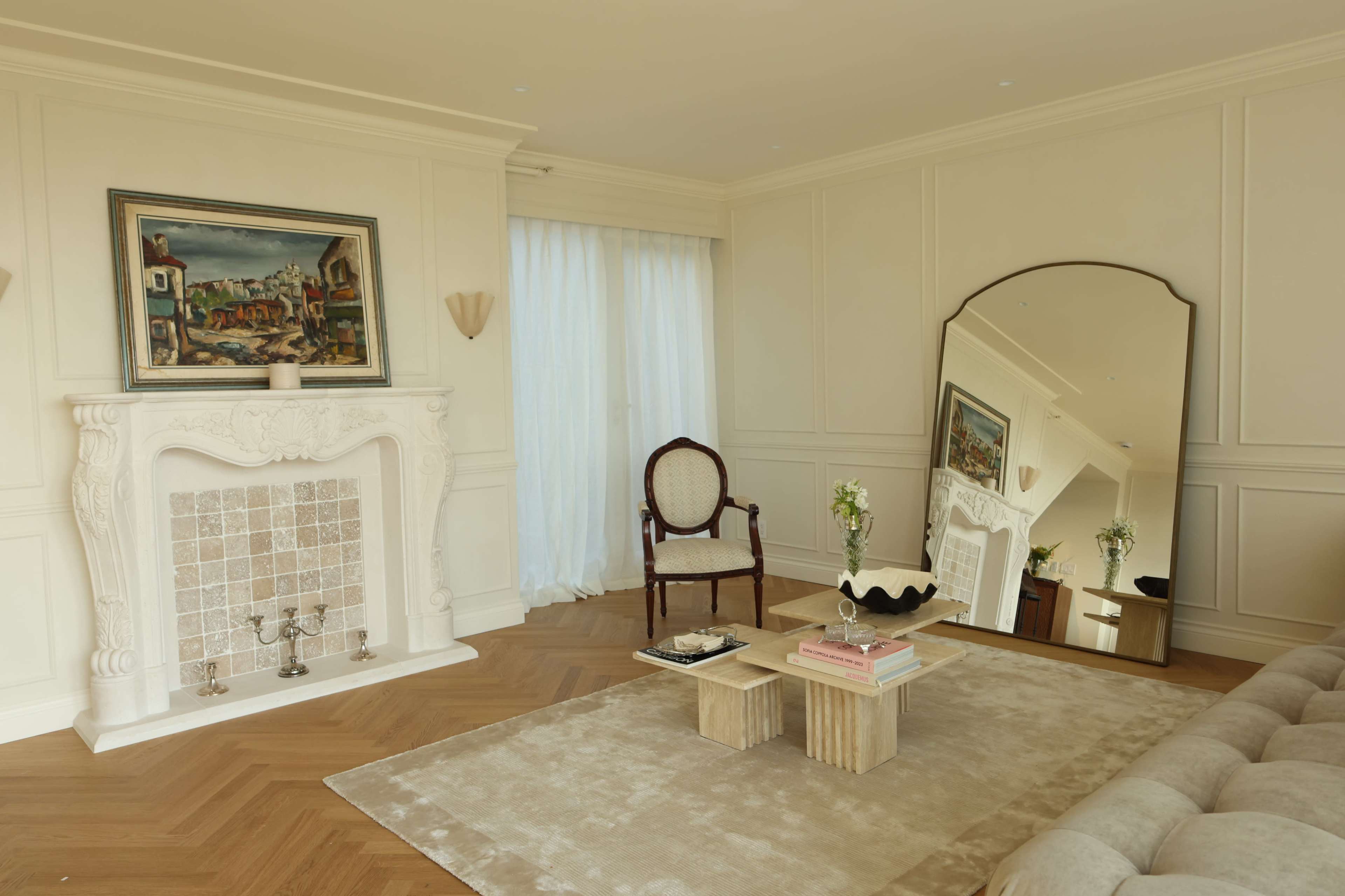 The image depicts a living room featuring a fireplace, a large mirror, a chair, and a coffee table on a plush rug.