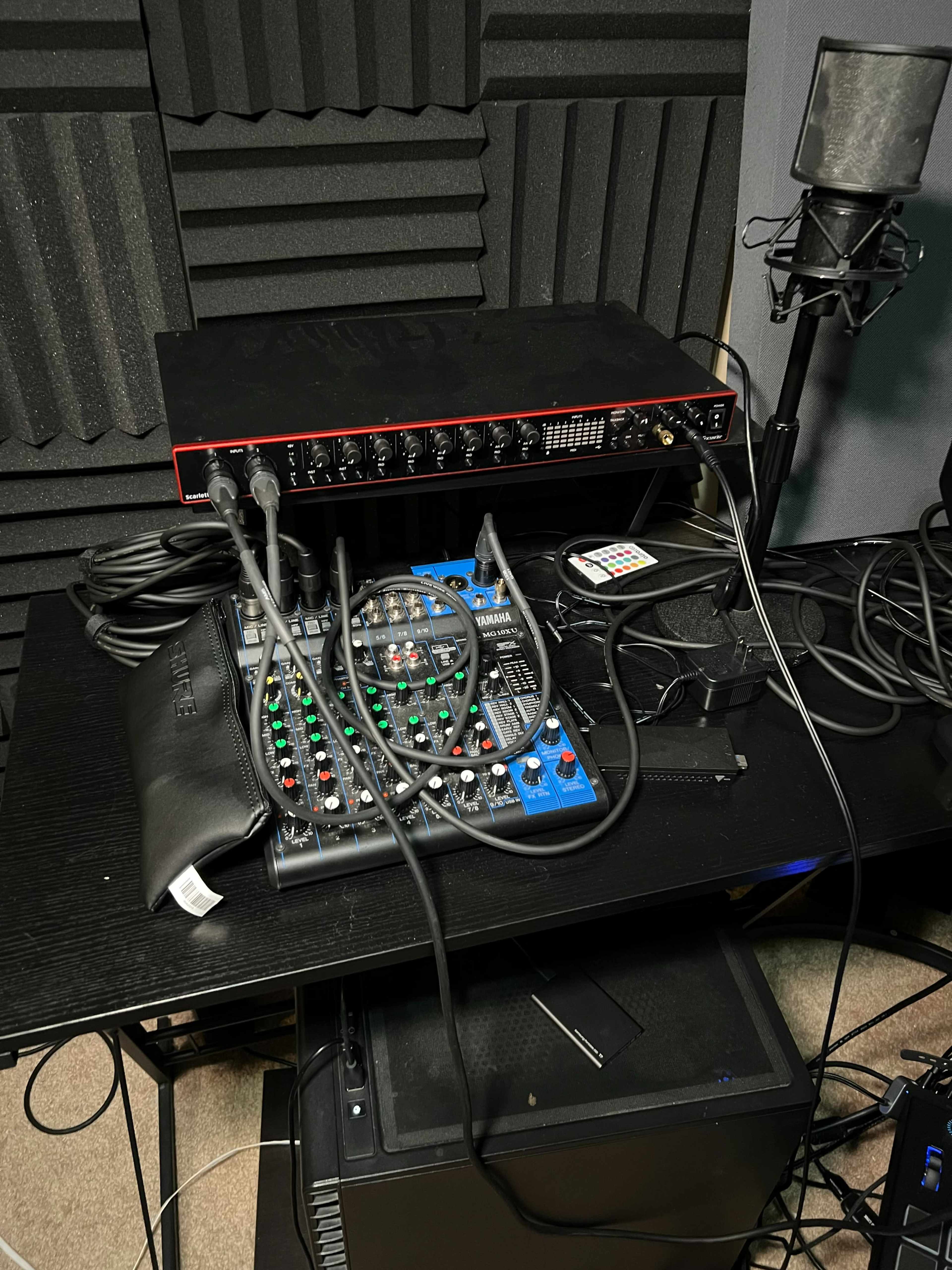 An audio mixing setup with a mixer and an interface on a black table, surrounded by soundproof foam panels.