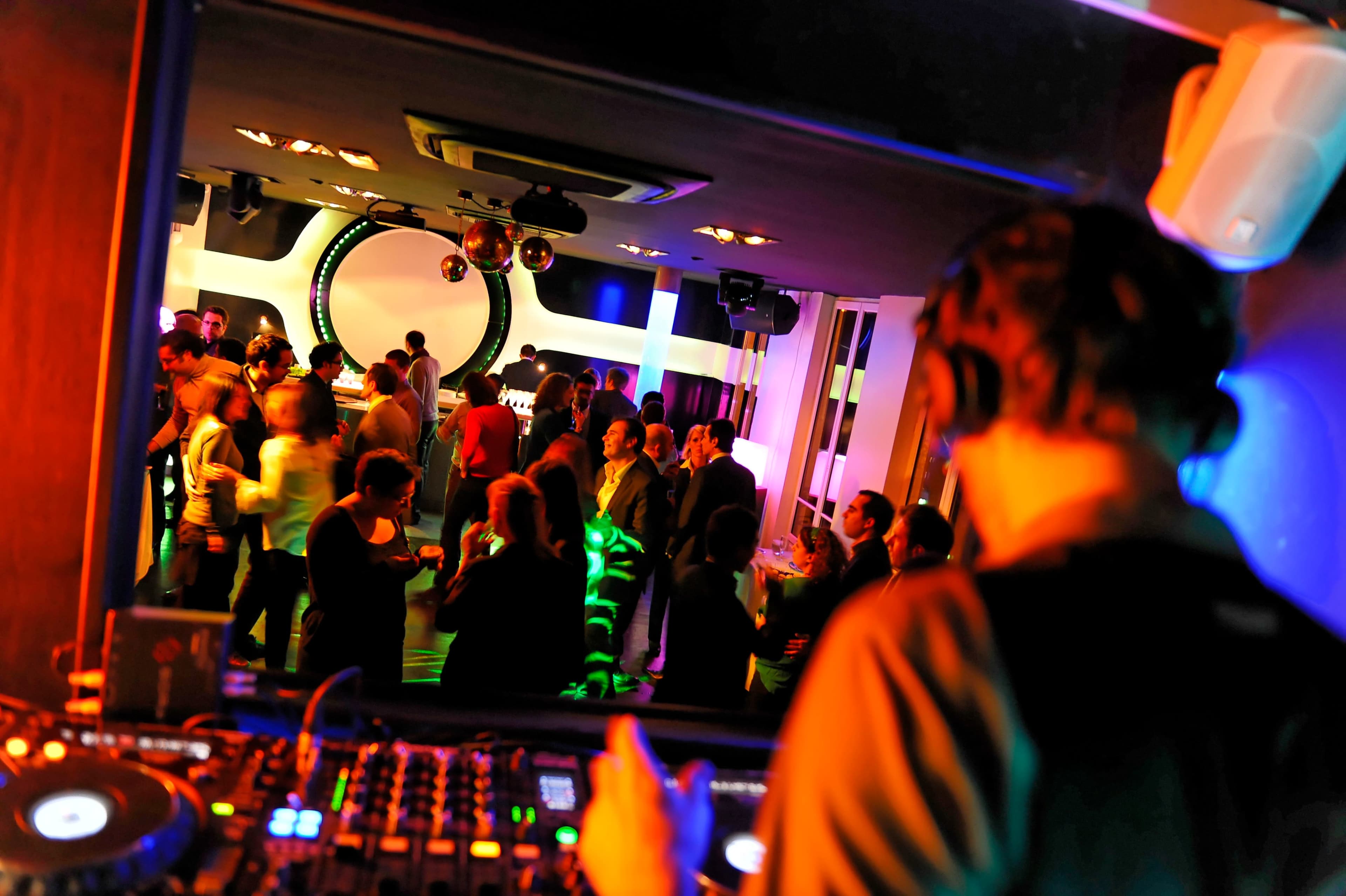 A DJ performs at a lively nightclub filled with dancing patrons and colorful lights.